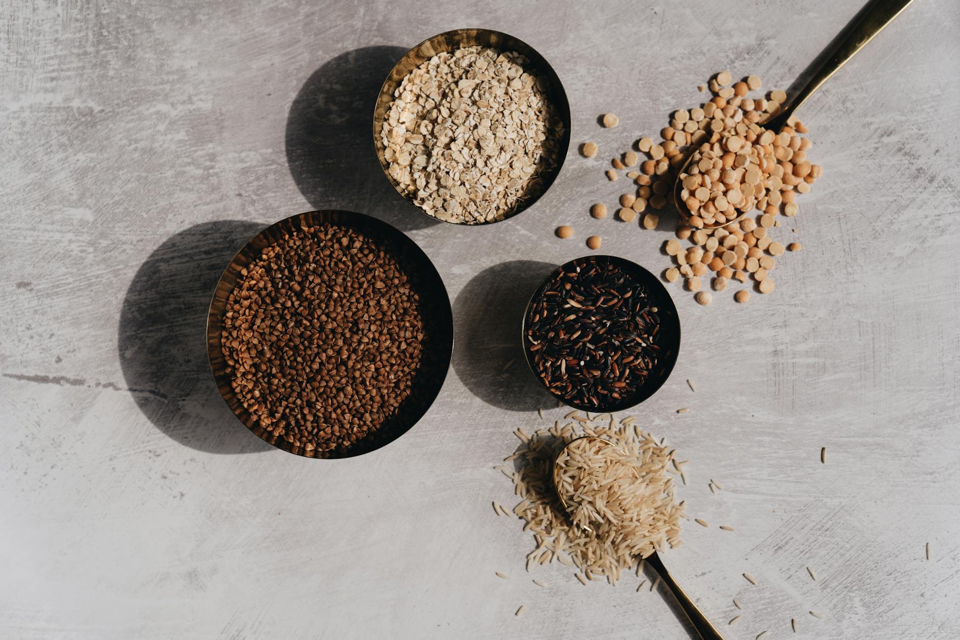 Flat lay of grains and pulses in bowls on a stone surface with shadows, perfect for food-related design. - protein fiber foods