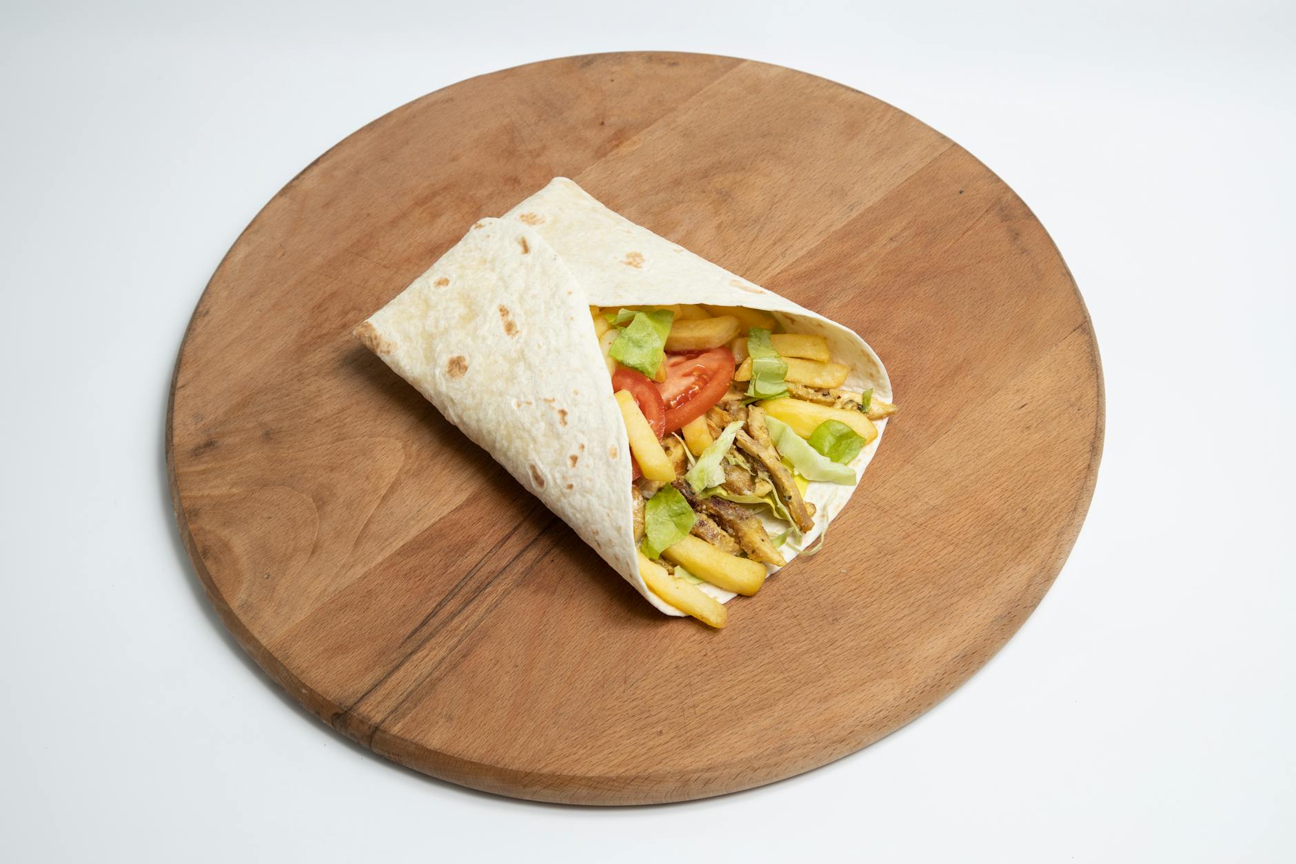 Close-up of a tortilla wrap filled with fries, lettuce, and tomatoes on a wooden board. - quick healthy dinners