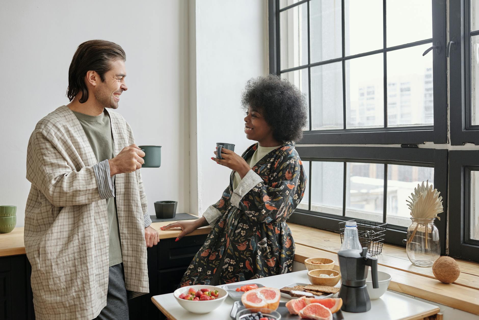 A happy couple enjoys morning coffee in a bright kitchen, sharing smiles and conversation. - seated good morning