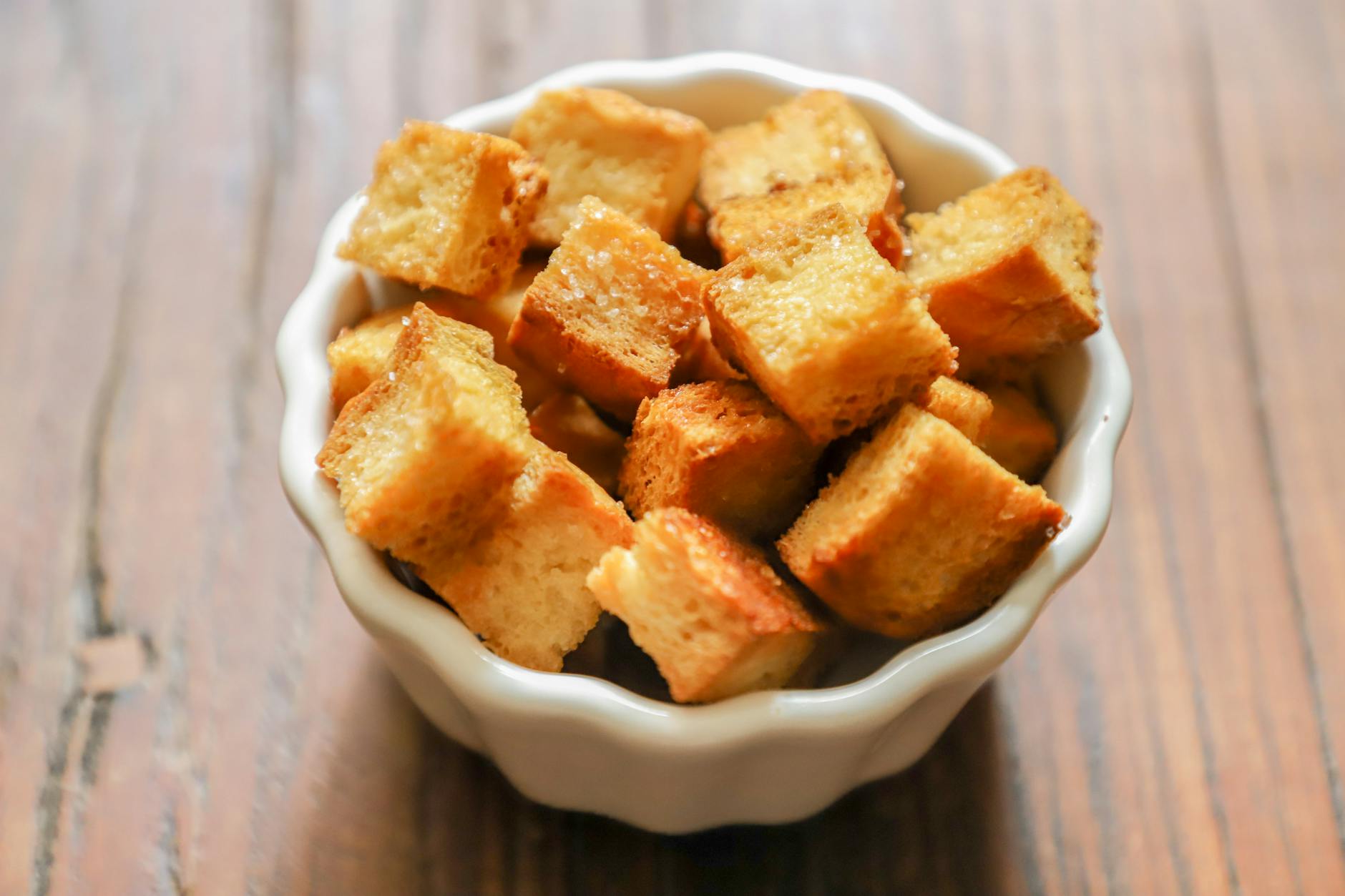 Close-up of golden-brown croutons in a white ceramic bowl on a rustic wooden table. - skinny recipes