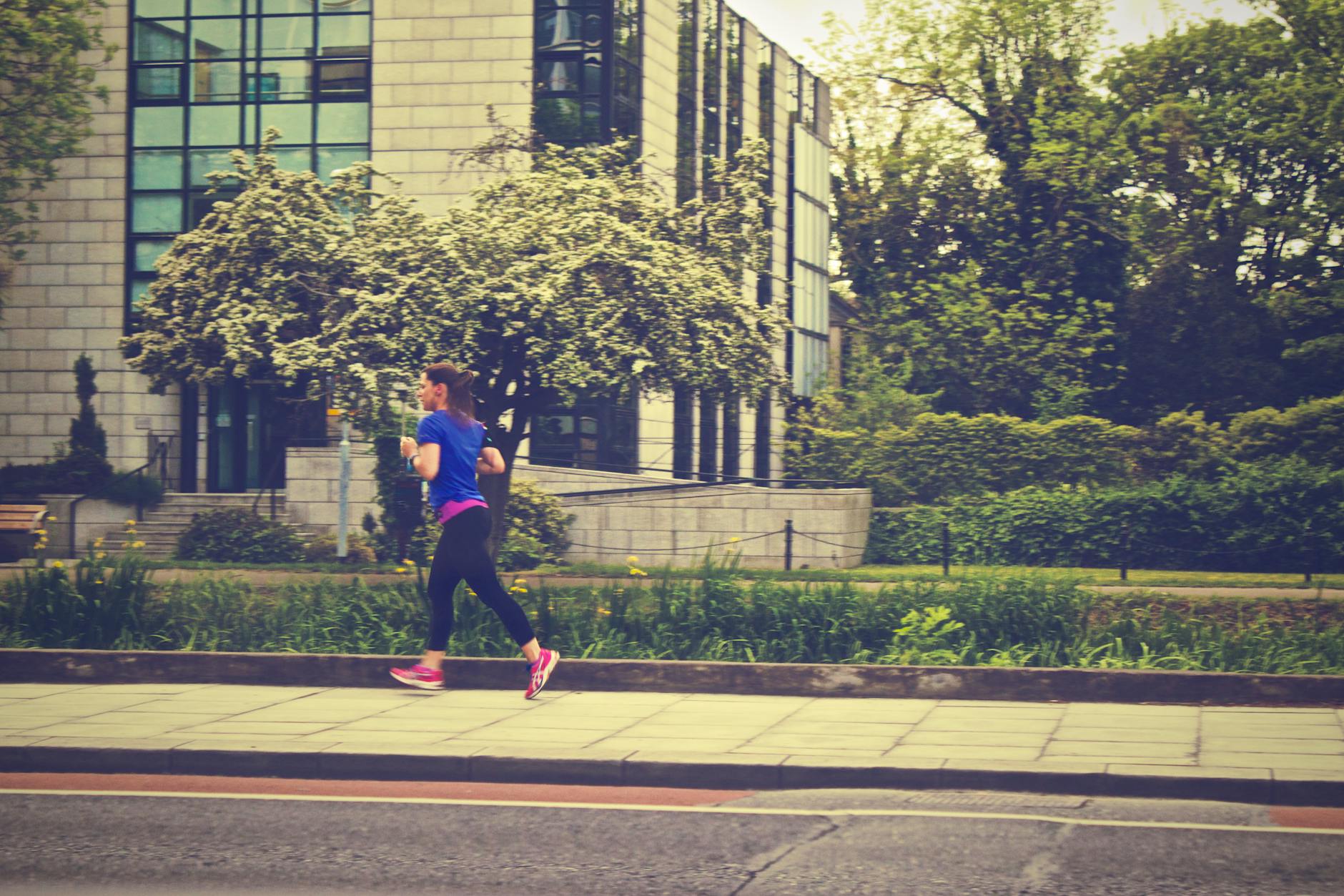 A woman running along a city street during the day surrounded by nature. - spring cardio outdoors