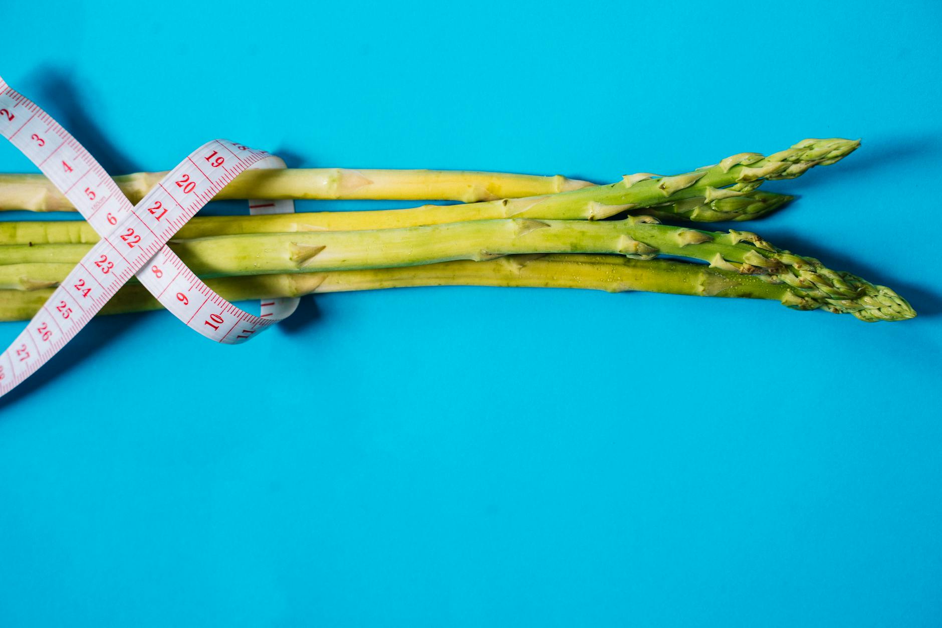 Fresh asparagus wrapped in a measuring tape against a bright blue background, symbolizing healthy eating. - spring diet reset