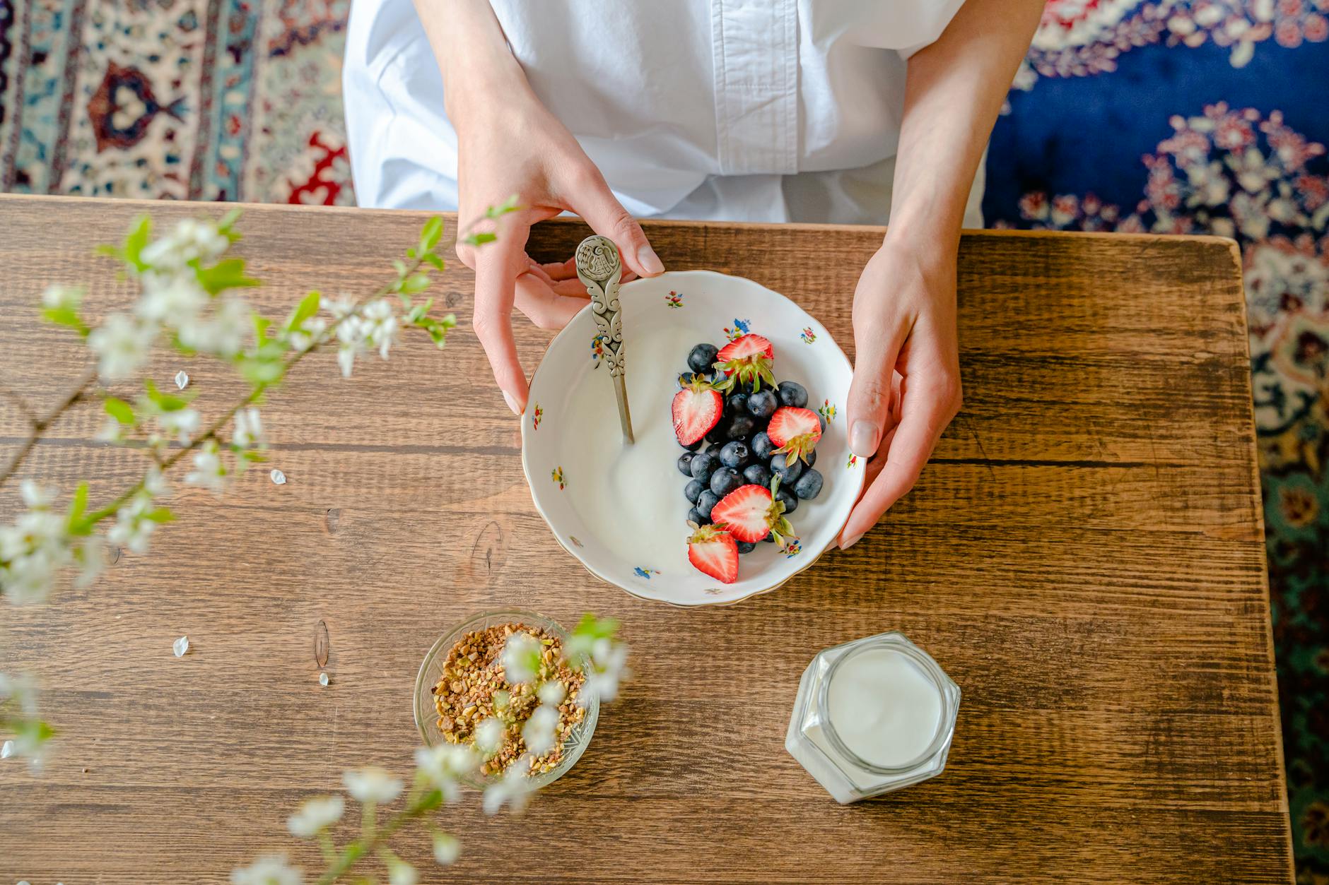 A top view of a person preparing a healthy breakfast with fresh berries, milk, and granola on a wooden table. - spring diet reset