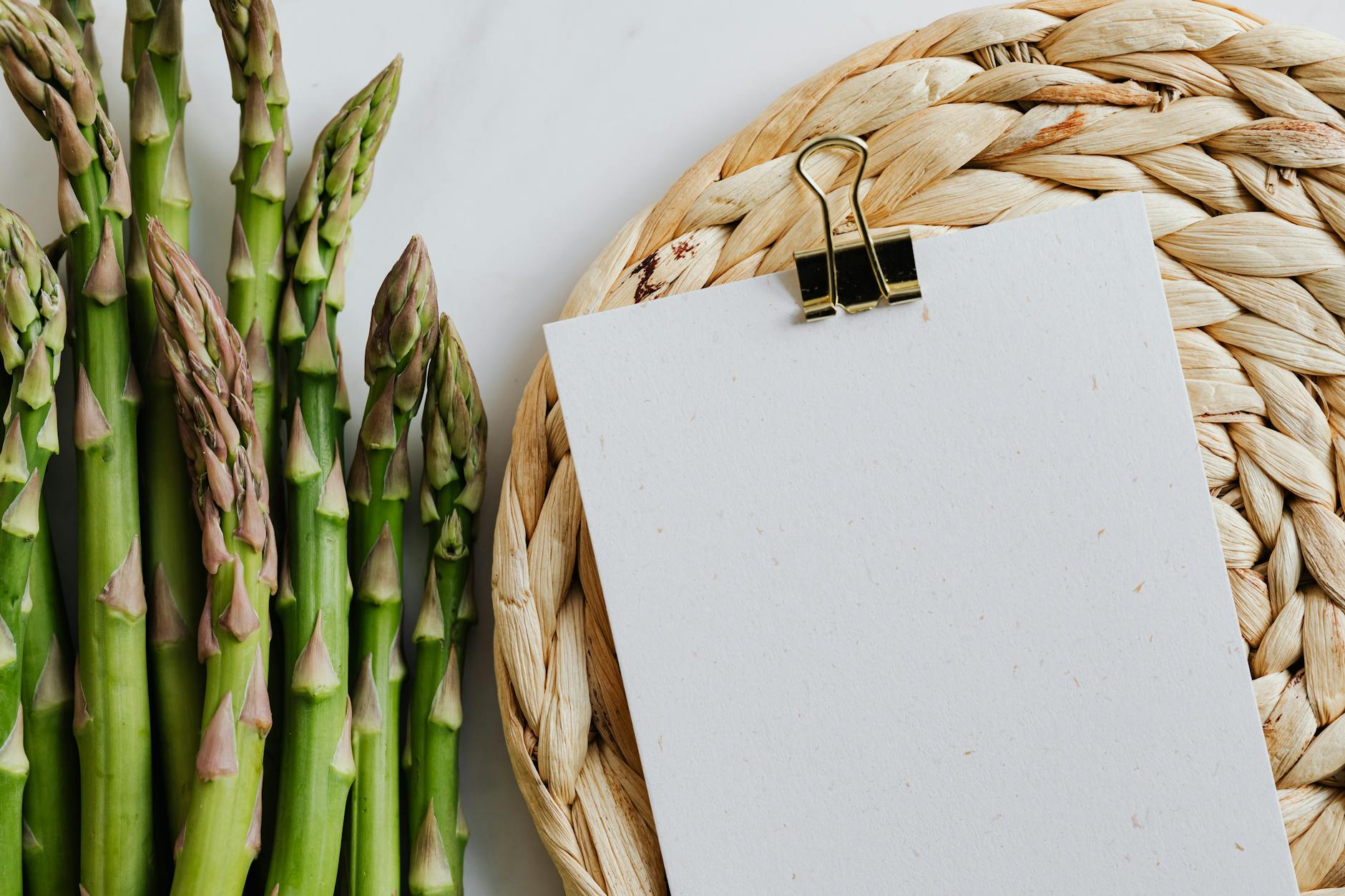 Fresh green asparagus beside a blank paper clip on a woven mat. Ideal for food or recipe concepts. - spring diet reset