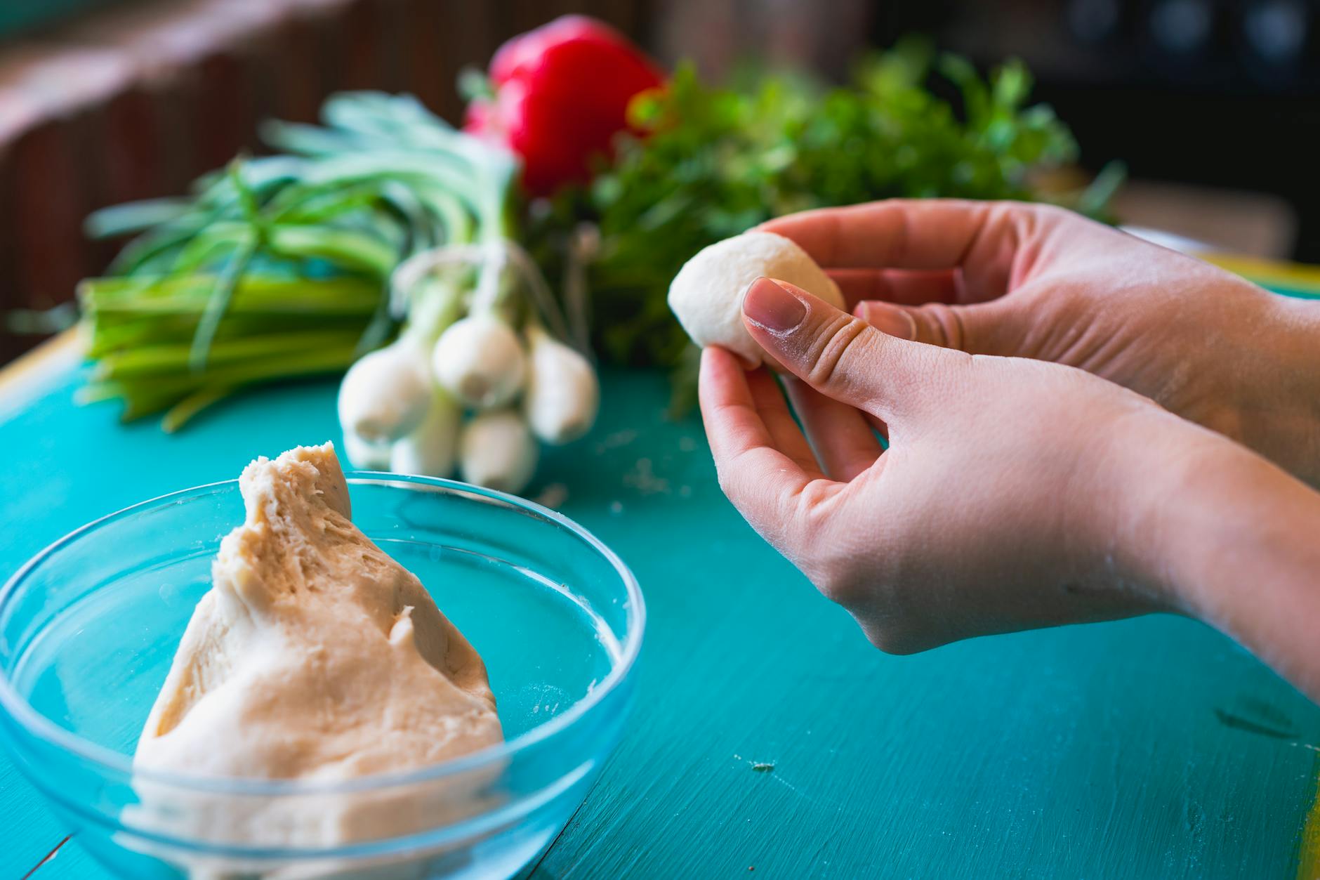 Close-up of hands shaping dough, with fresh vegetables in the background on a kitchen countertop. - spring meal prep