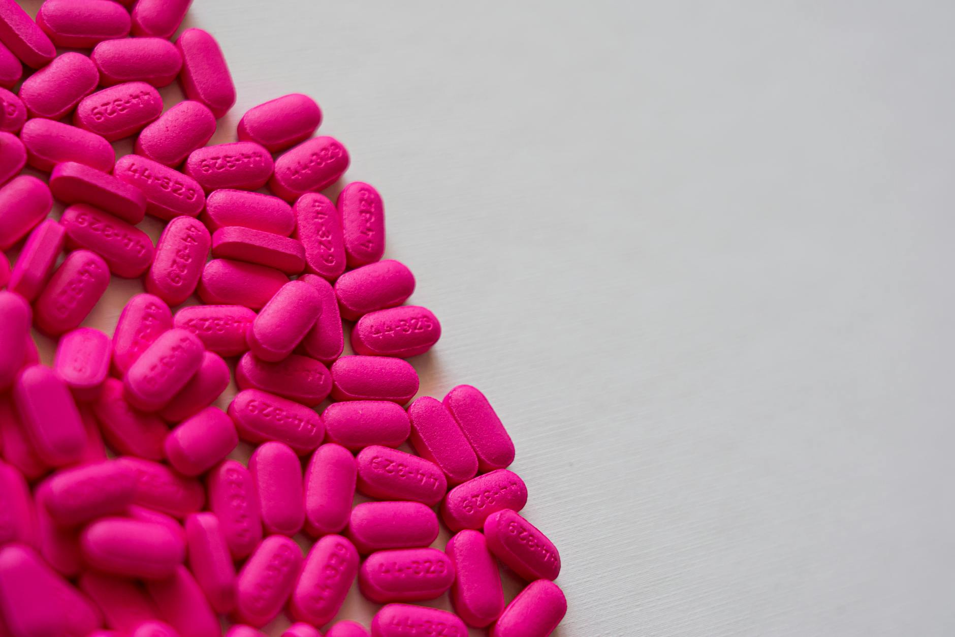 Close-up of vibrant pink pills scattered on a white surface. - spring pollen allergies