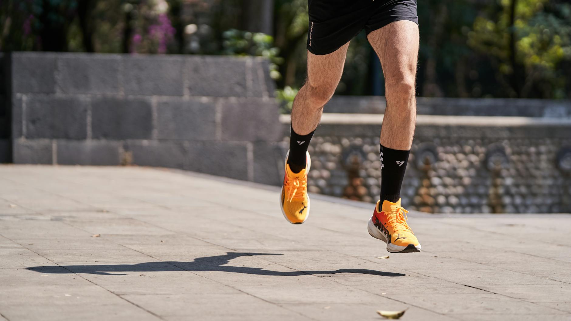 Male runner with orange shoes sprinting outdoors on a sunny day, showing athleticism. - spring trail running