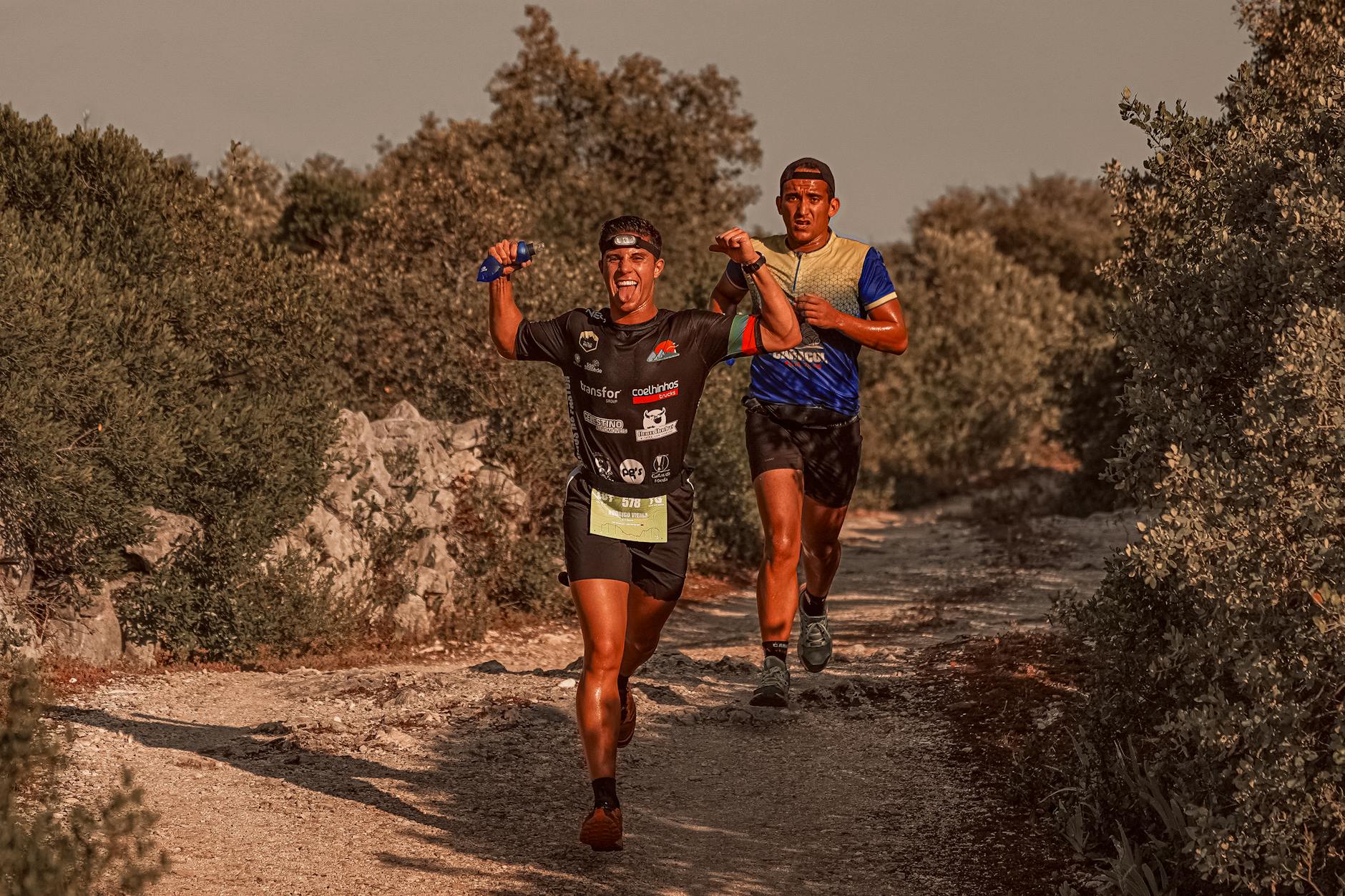 Two athletes express joy during a rural marathon run, surrounded by shrubs. - spring trail running