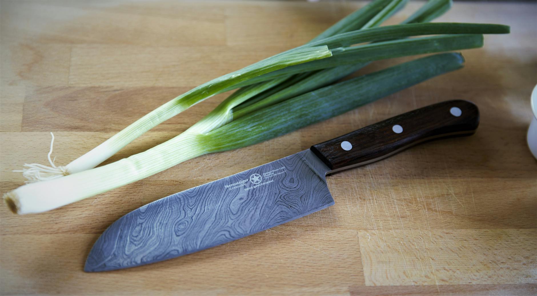 Close-up of a chef's knife and spring onions on a wooden cutting board. - spring vegetable recipes