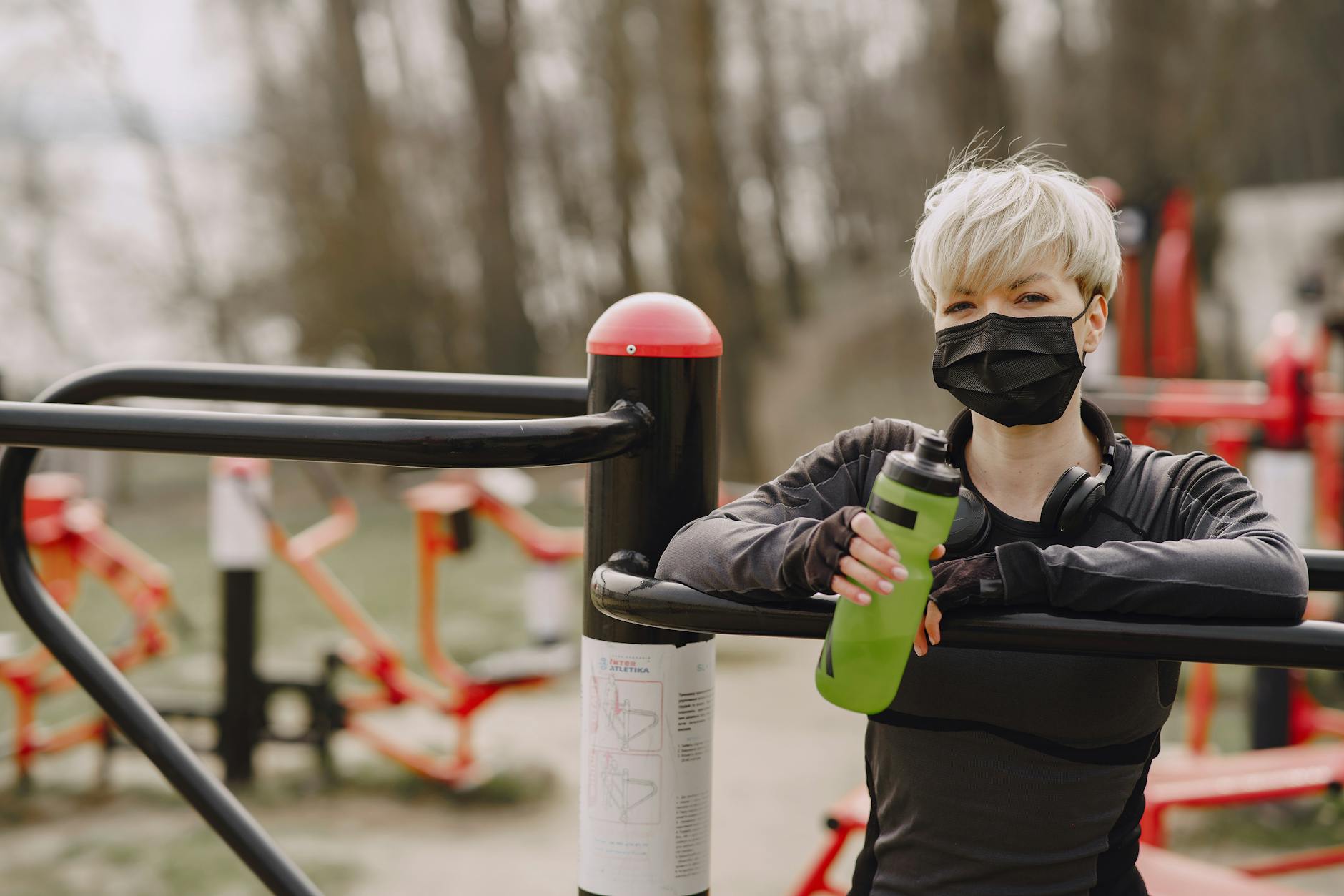 Woman in outdoor fitness setting wearing mask, holding water bottle, demonstrating pandemic safety. - spring workout refresh