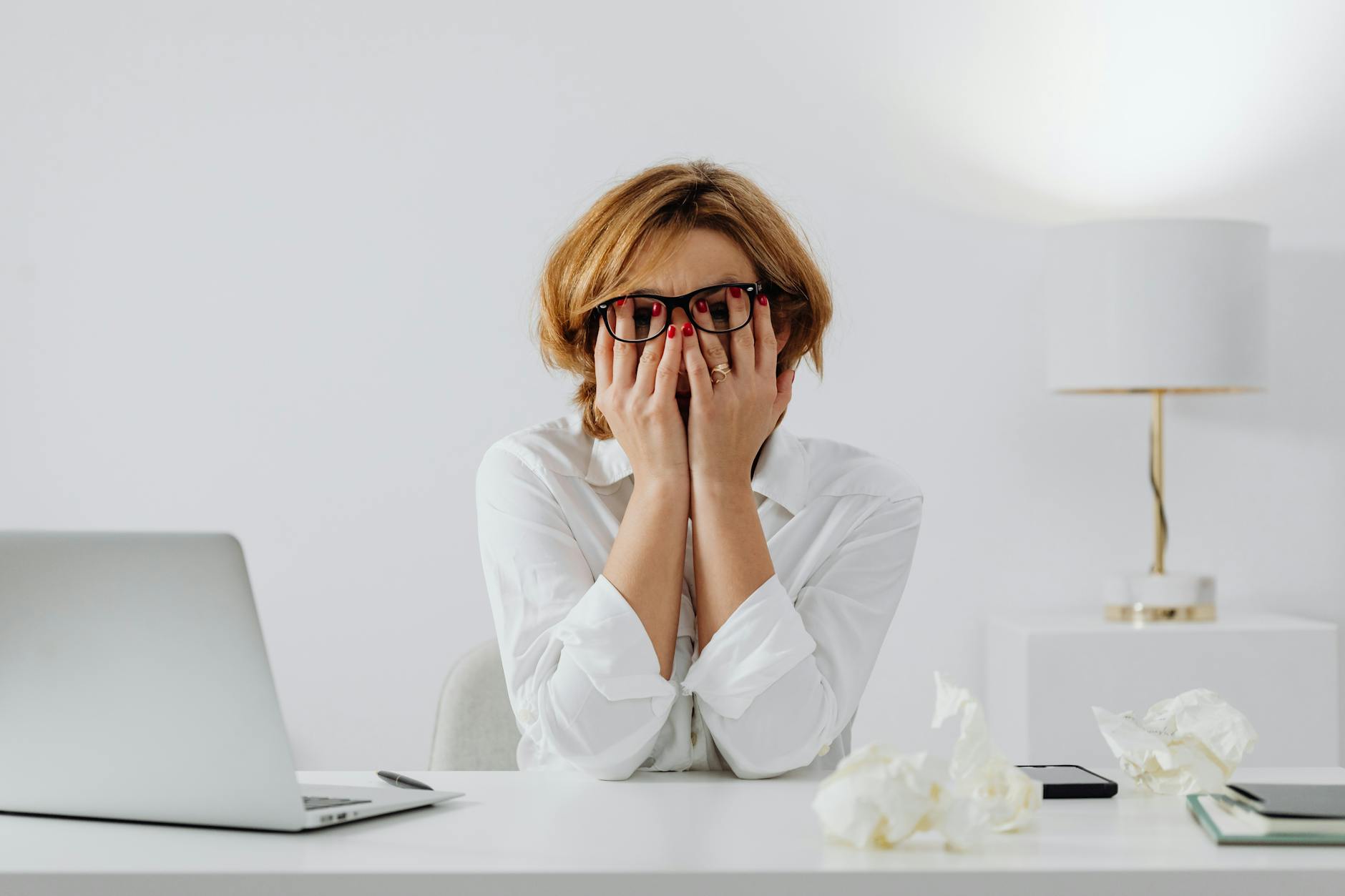 Woman with hands on face, sitting at desk with laptop and tissues, feeling stressed. - stress management techniques