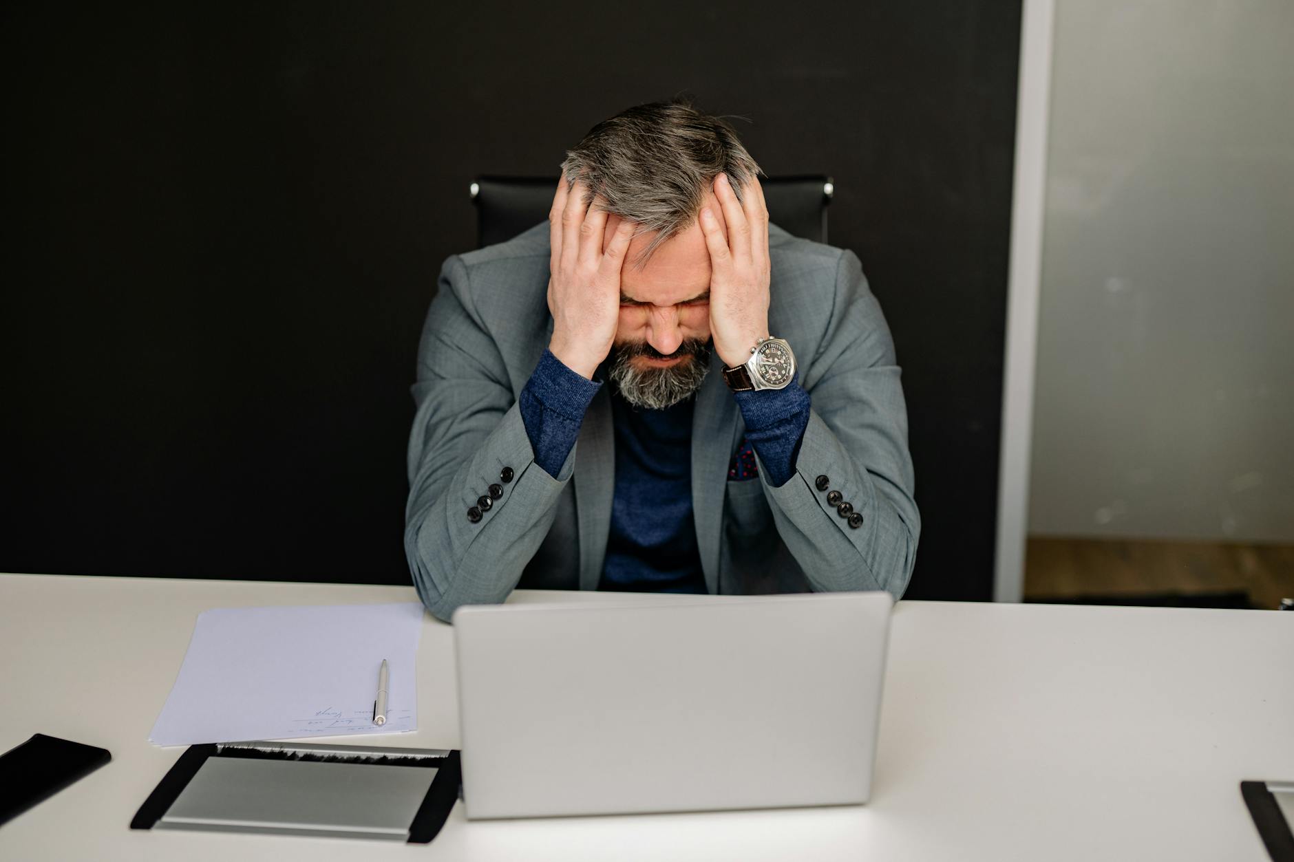 Businessman showing frustration with hands on head while working on a laptop in an office setting. - stress management techniques