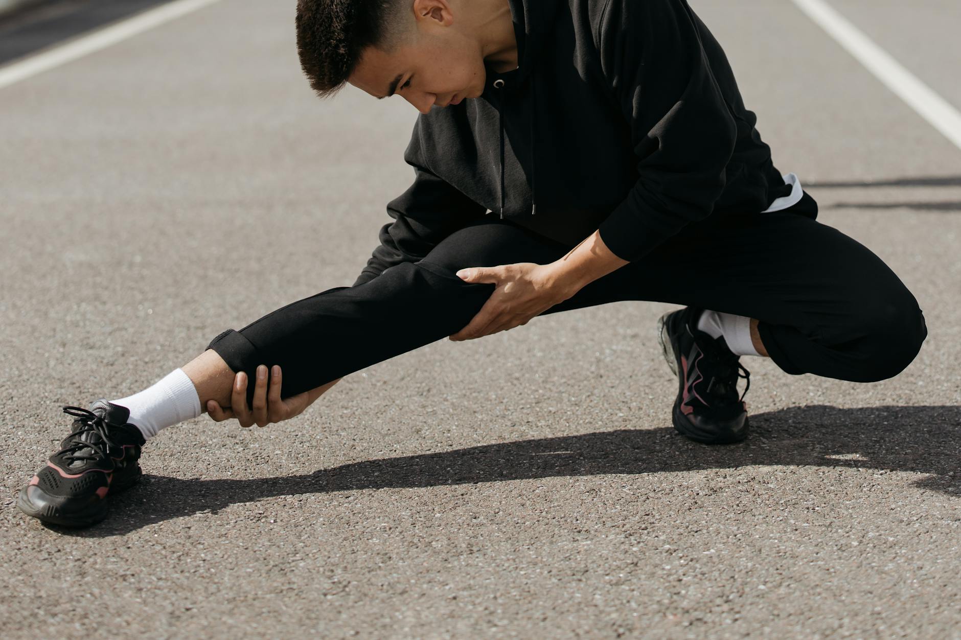 A young man performs stretching exercises on a city street, focusing on flexibility and fitness. - stretching routine men