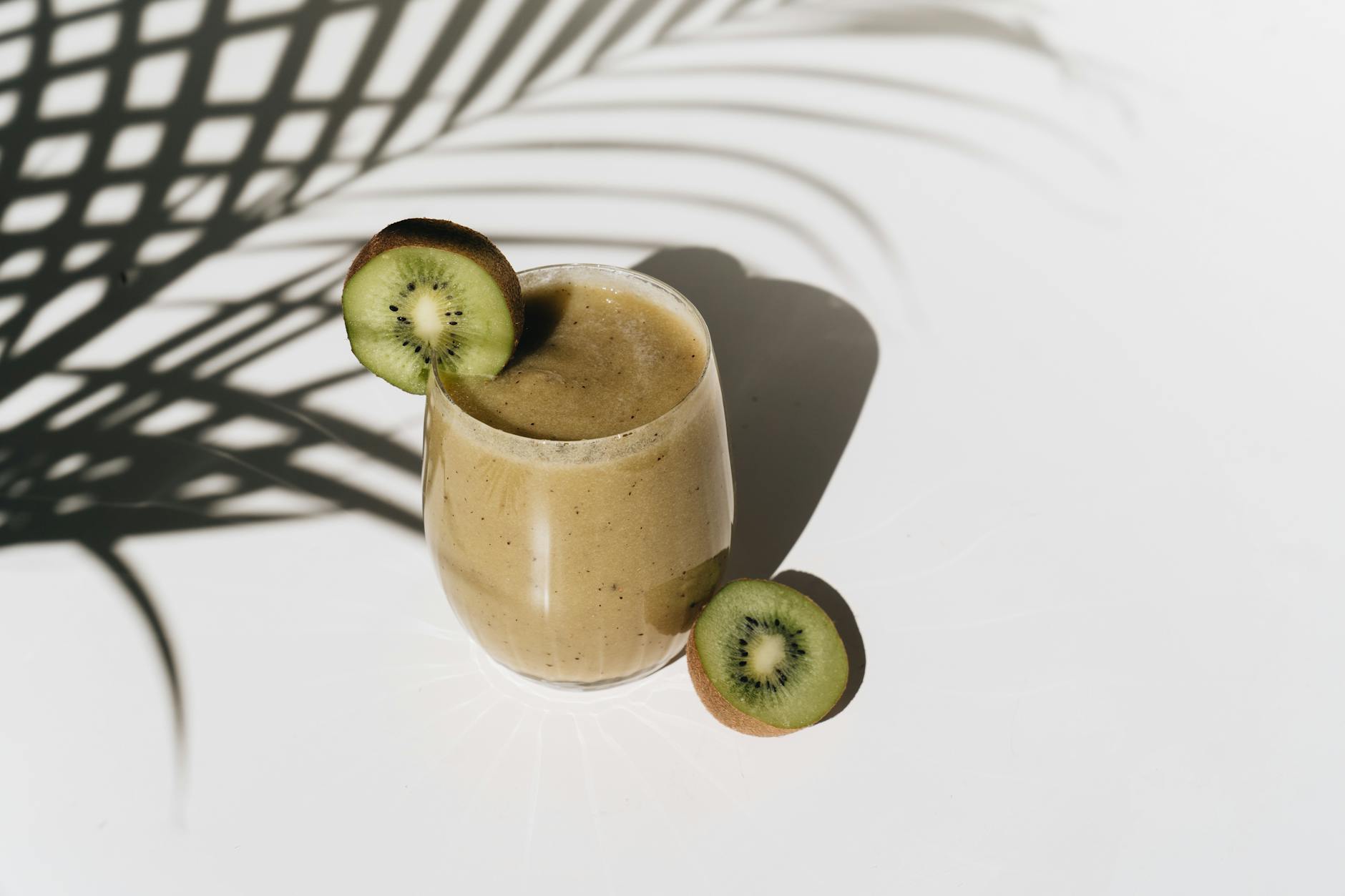 A vibrant kiwi smoothie with palm leaf shadows creating a tropical feel. - sunlight mood boost
