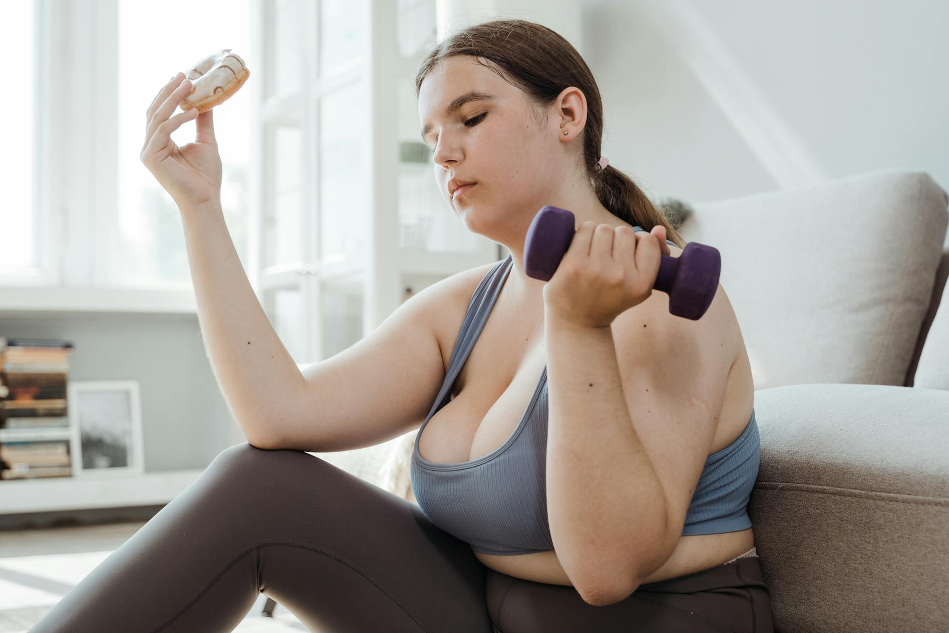 A plus size woman in activewear balancing a dumbbell and a donut, symbolizing fitness and indulgence. - sustainable weight loss