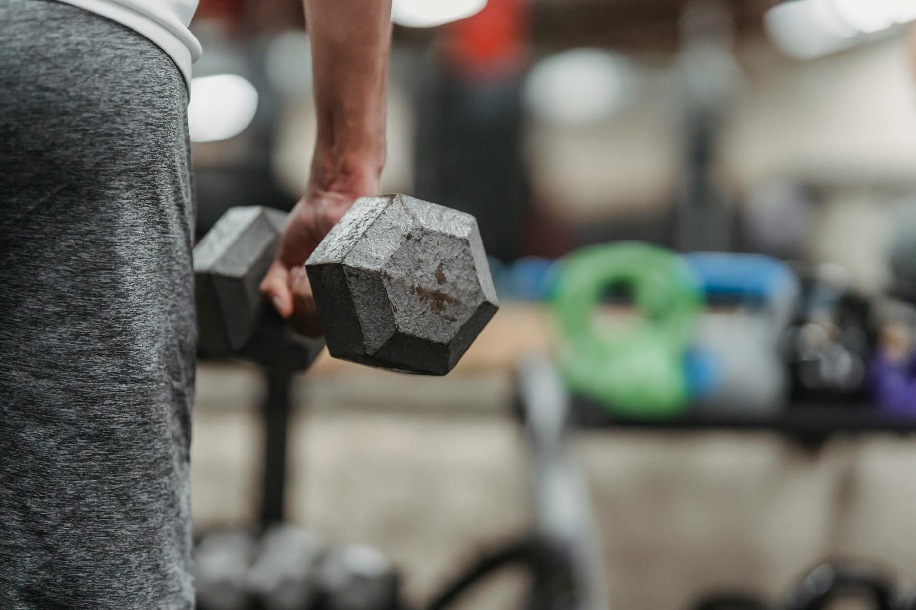 Focused view of a male athlete lifting a dumbbell in a gym setting for strength training. - treadmill fat burn