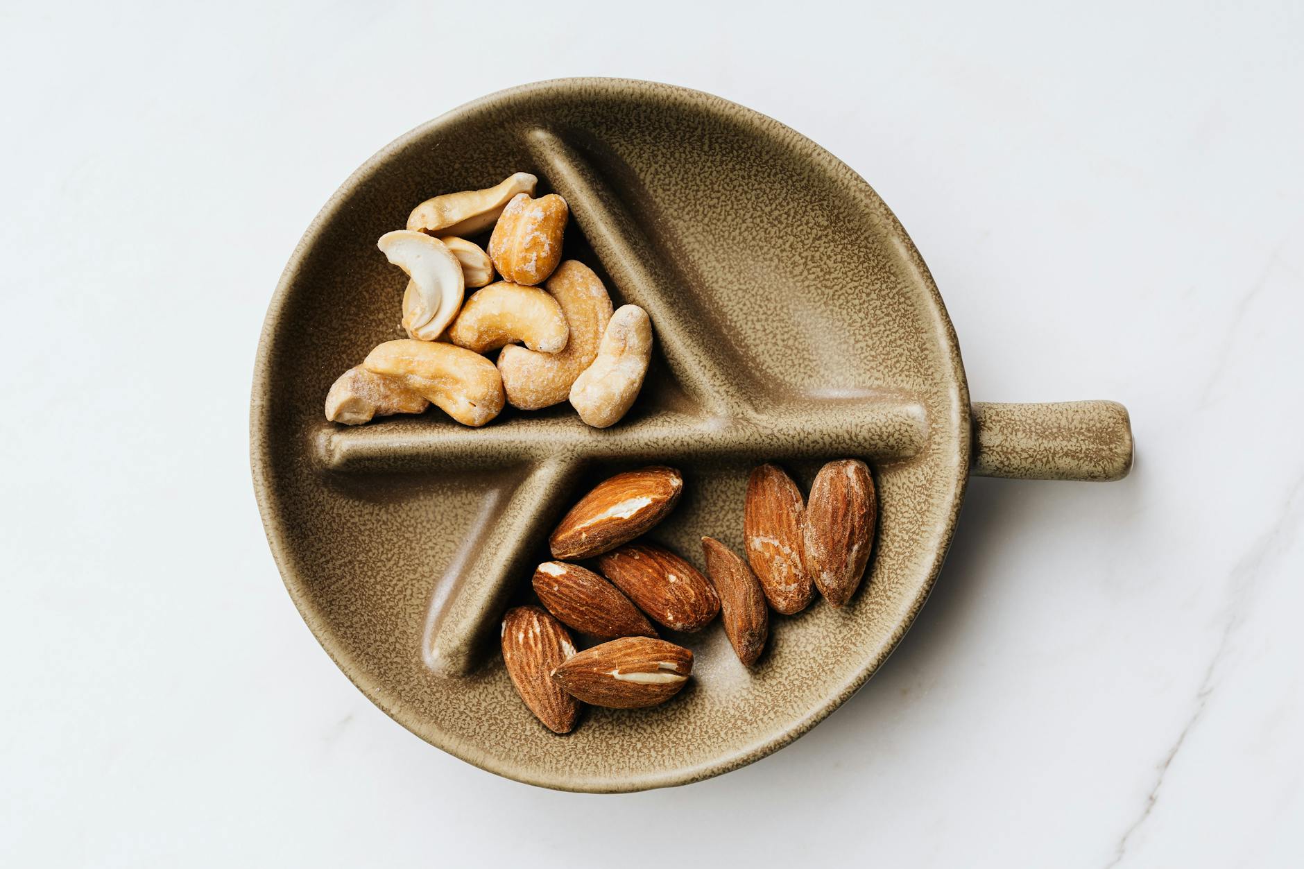 Assortment of cashews and almonds presented on a decorative ceramic plate against a clean white background. - vegan protein sources