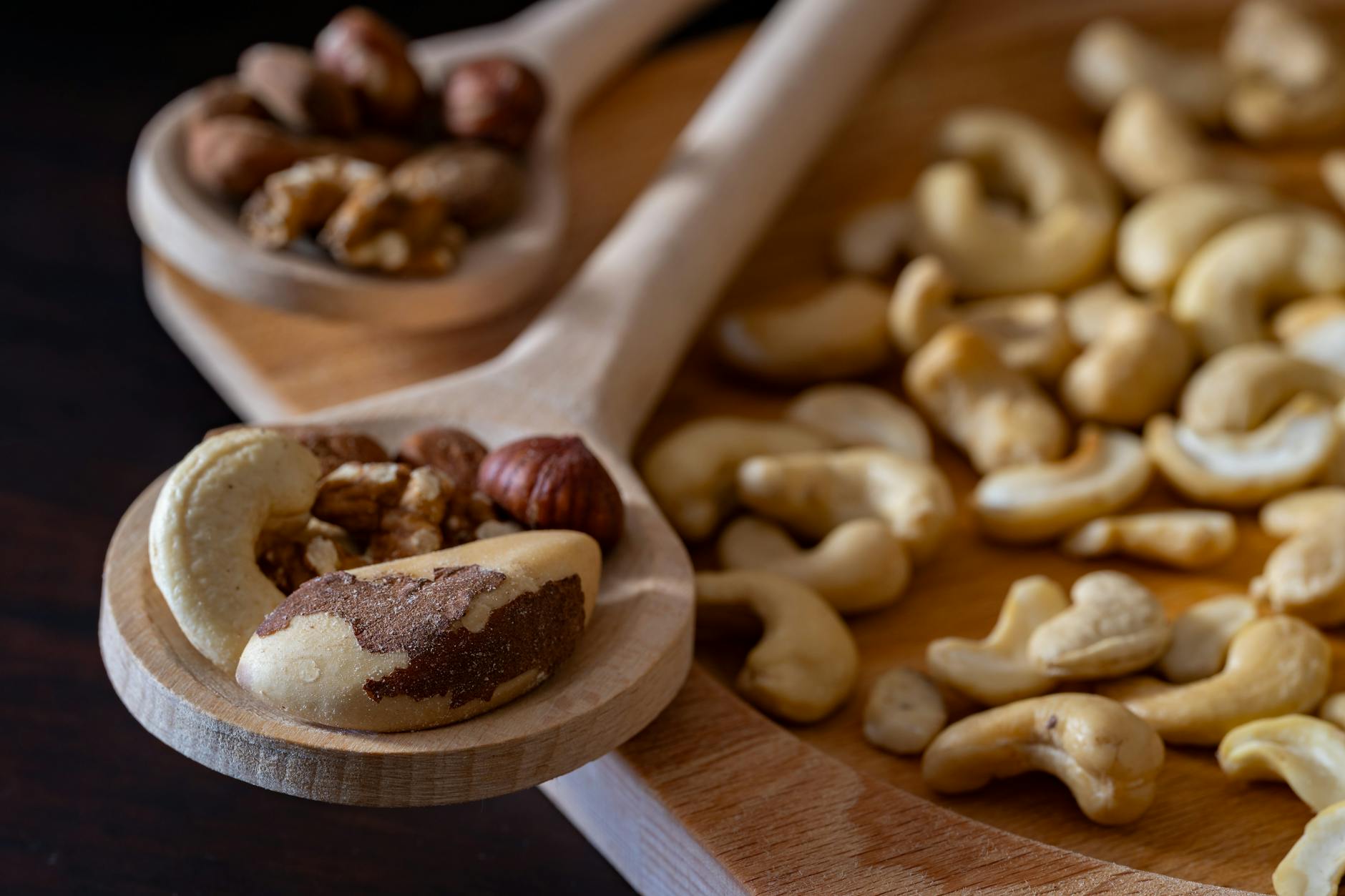 Close-up of mixed nuts including almonds, cashews, and walnuts on wooden spoons, ideal for healthy snacking. - vegan protein sources