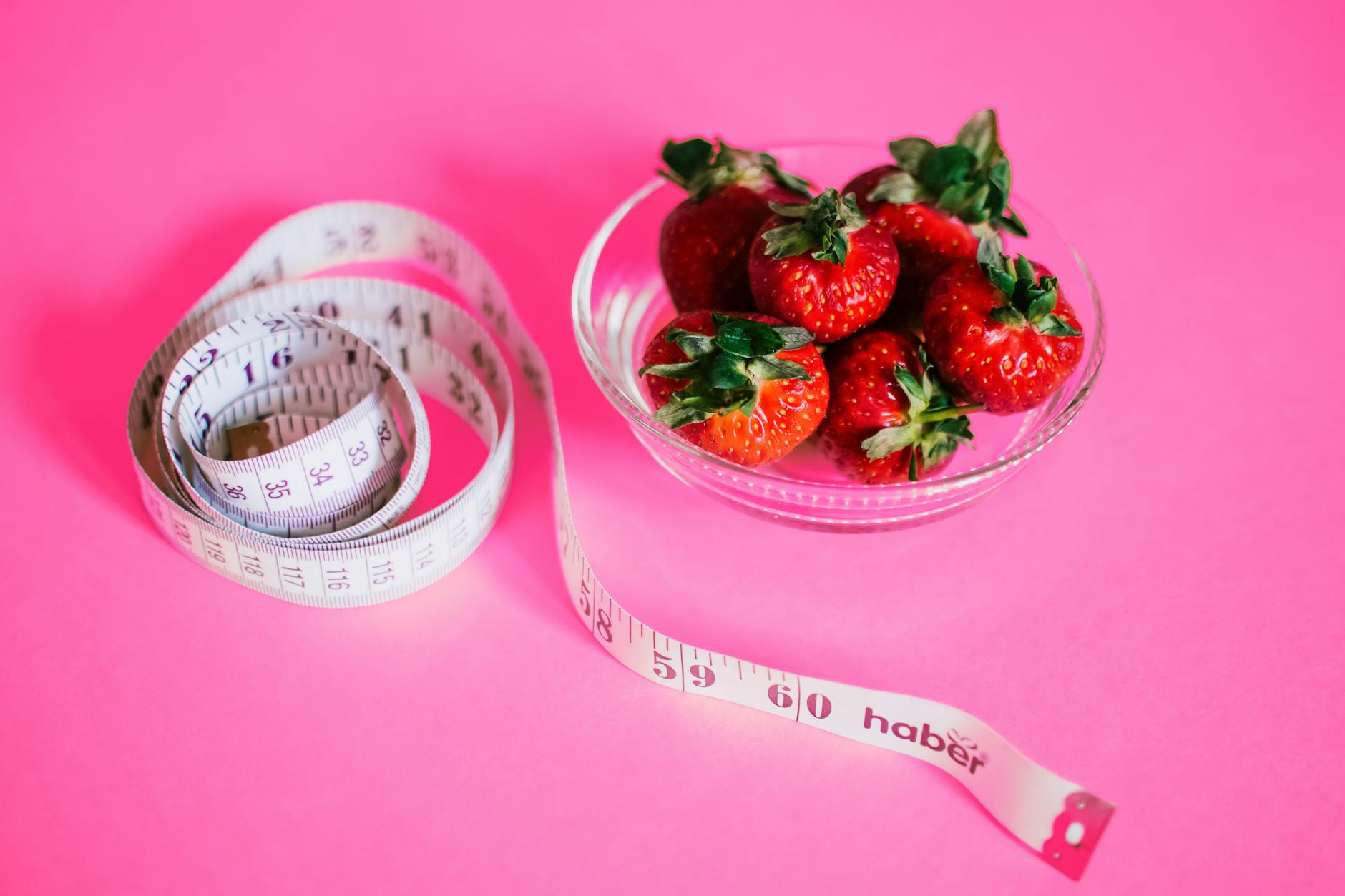 A glass bowl of fresh strawberries paired with a pink measuring tape symbolizes healthy eating. - walk for weight loss