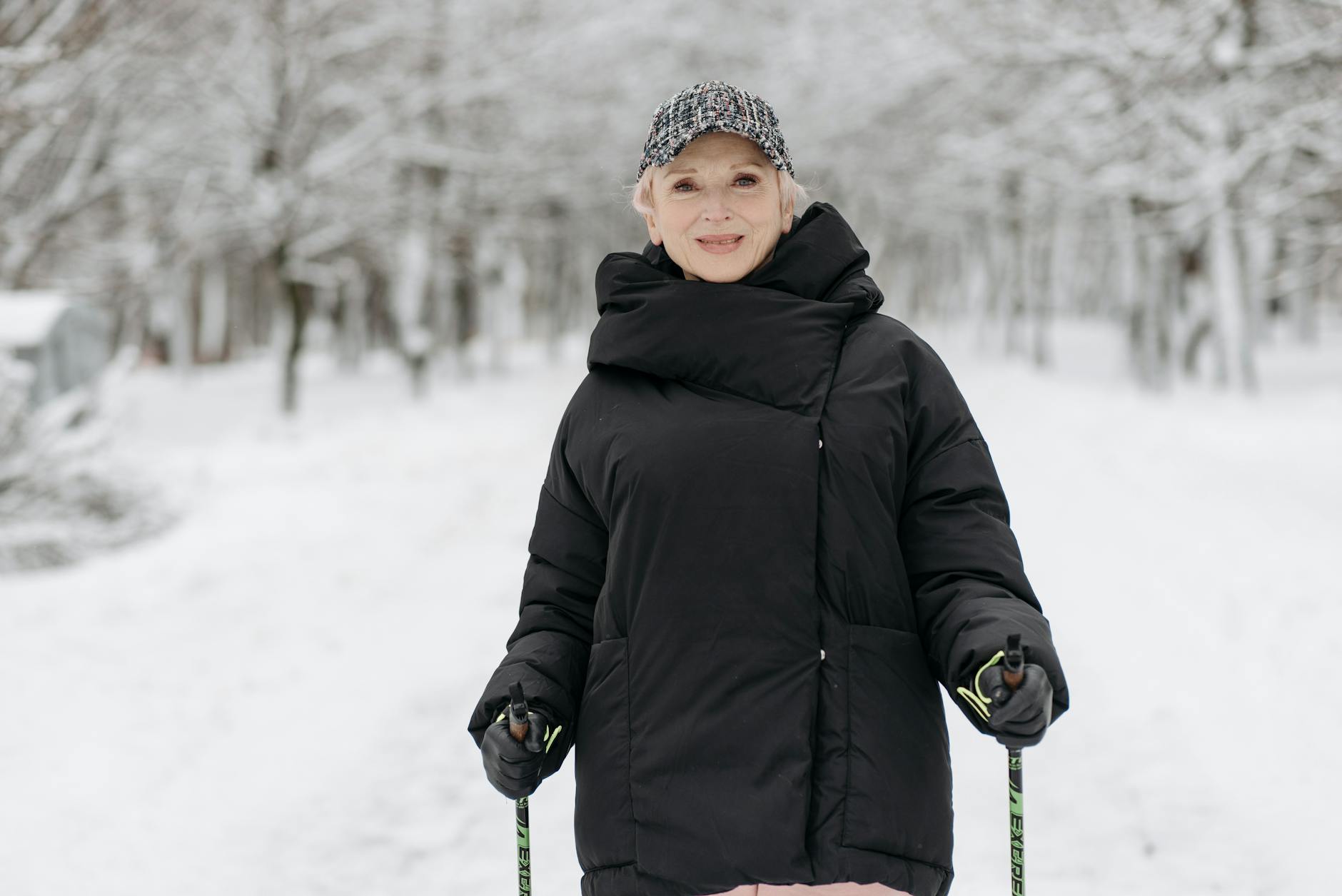 Senior woman enjoying a winter walk with ski poles in a snowy park, dressed in warm attire. - winter wellness slump
