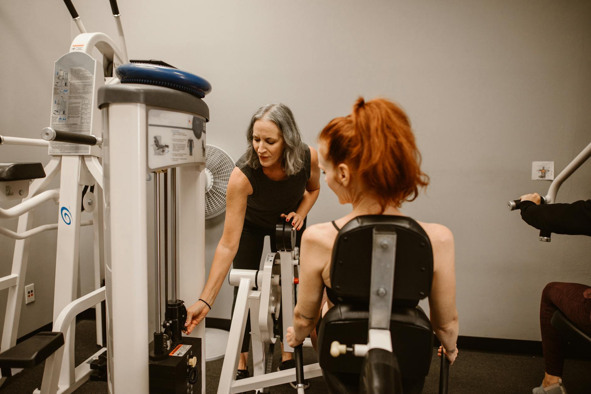 A personal trainer guides a woman using gym equipment, promoting healthy living. - women's gym workout