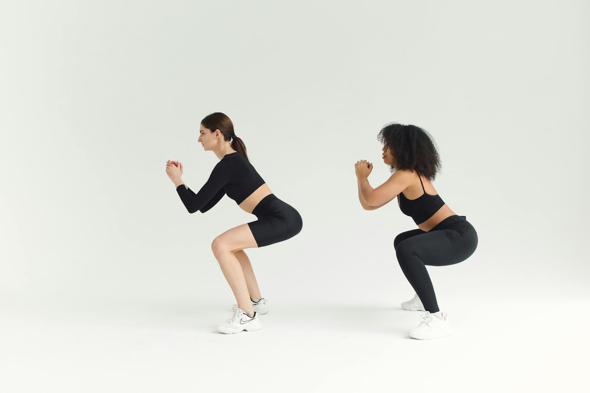 Two women performing squats in sportswear against a plain background, emphasizing fitness and a healthy lifestyle. - 30 minute workout