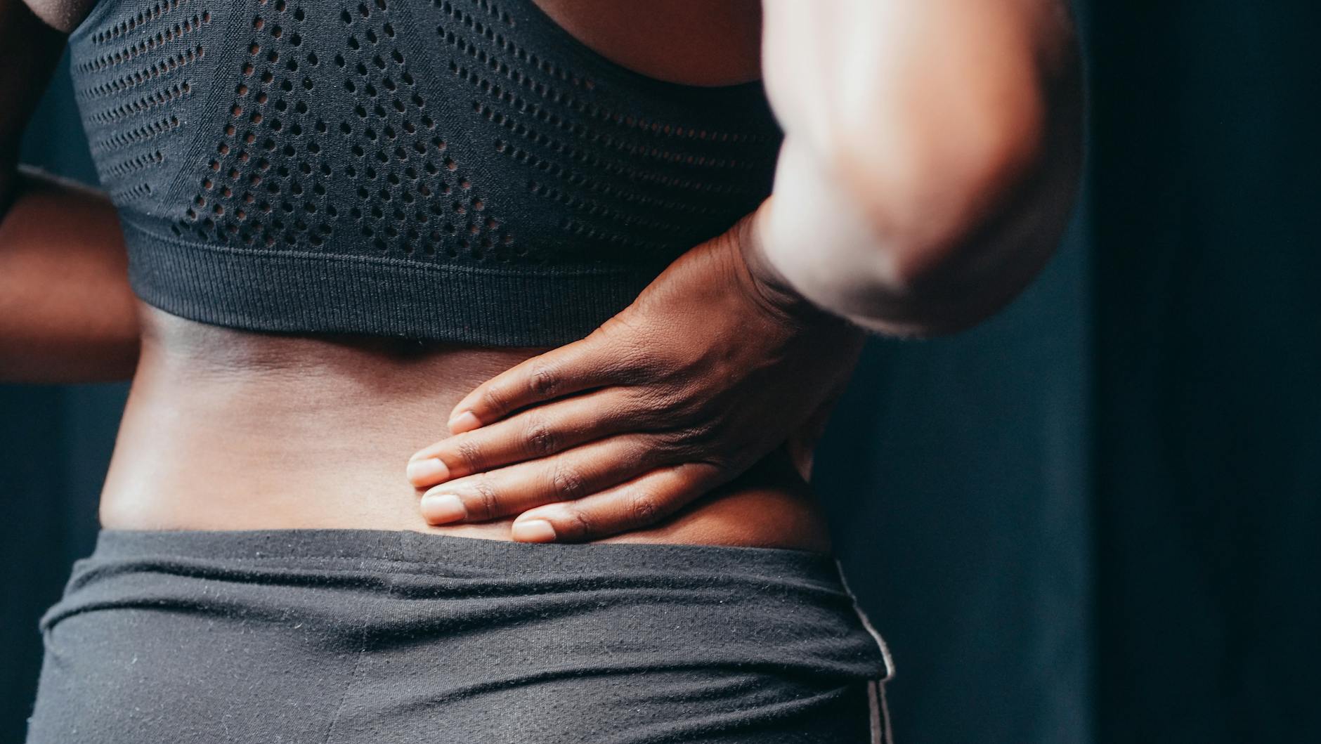 An adult of African descent holding their lower back in pain, indicating discomfort or injury. - back pain causes