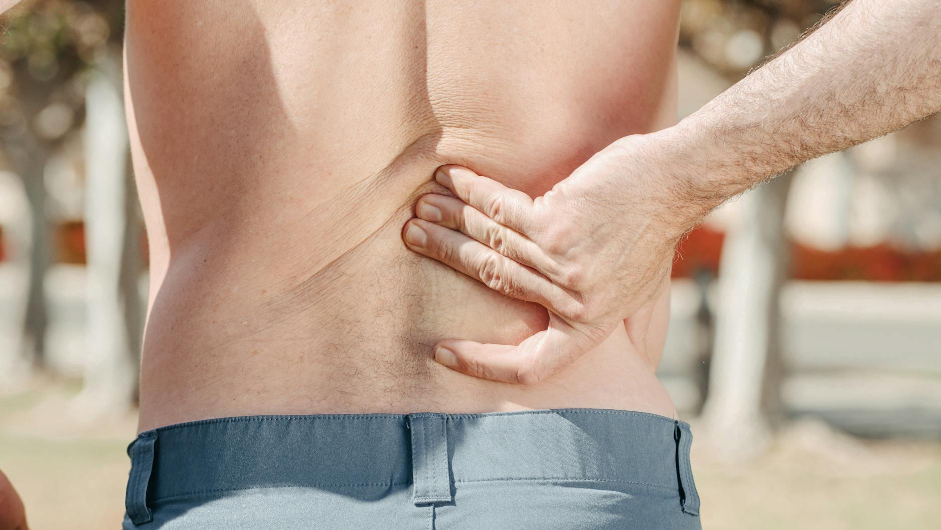 Close-up of a man holding his lower back in pain, possibly indicating discomfort or injury. - back pain causes