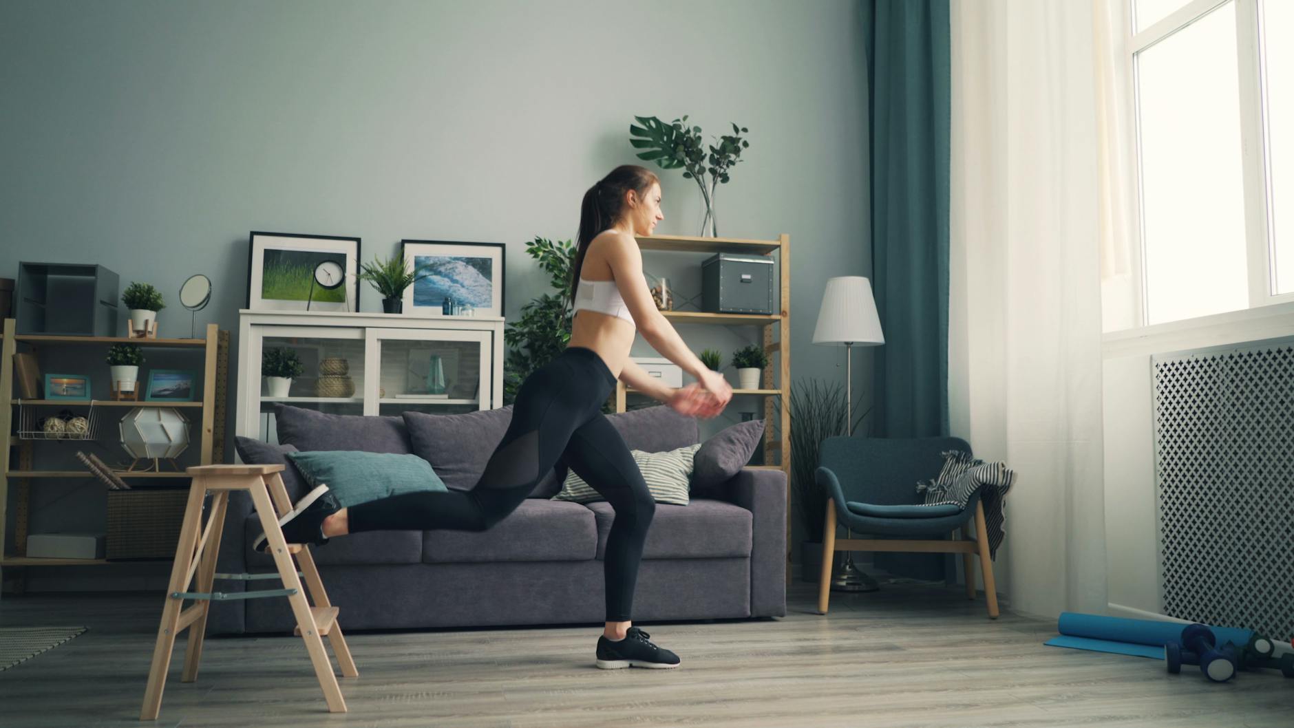 A woman in sportswear working out indoors using a chair for support, demonstrating leg exercises. - balance exercises