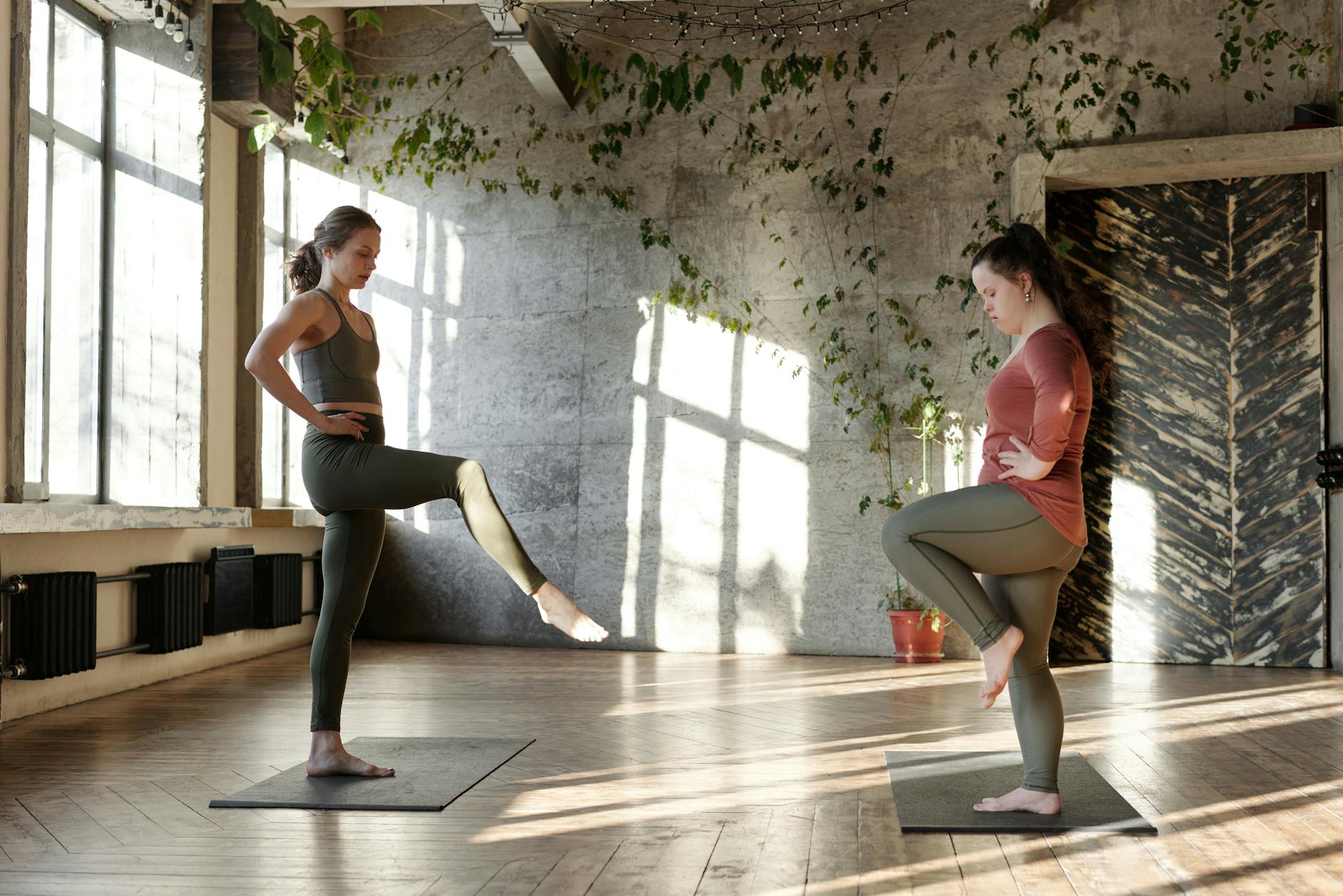 Two women in a sunlit studio practicing yoga with concentration and balance. - balance exercises