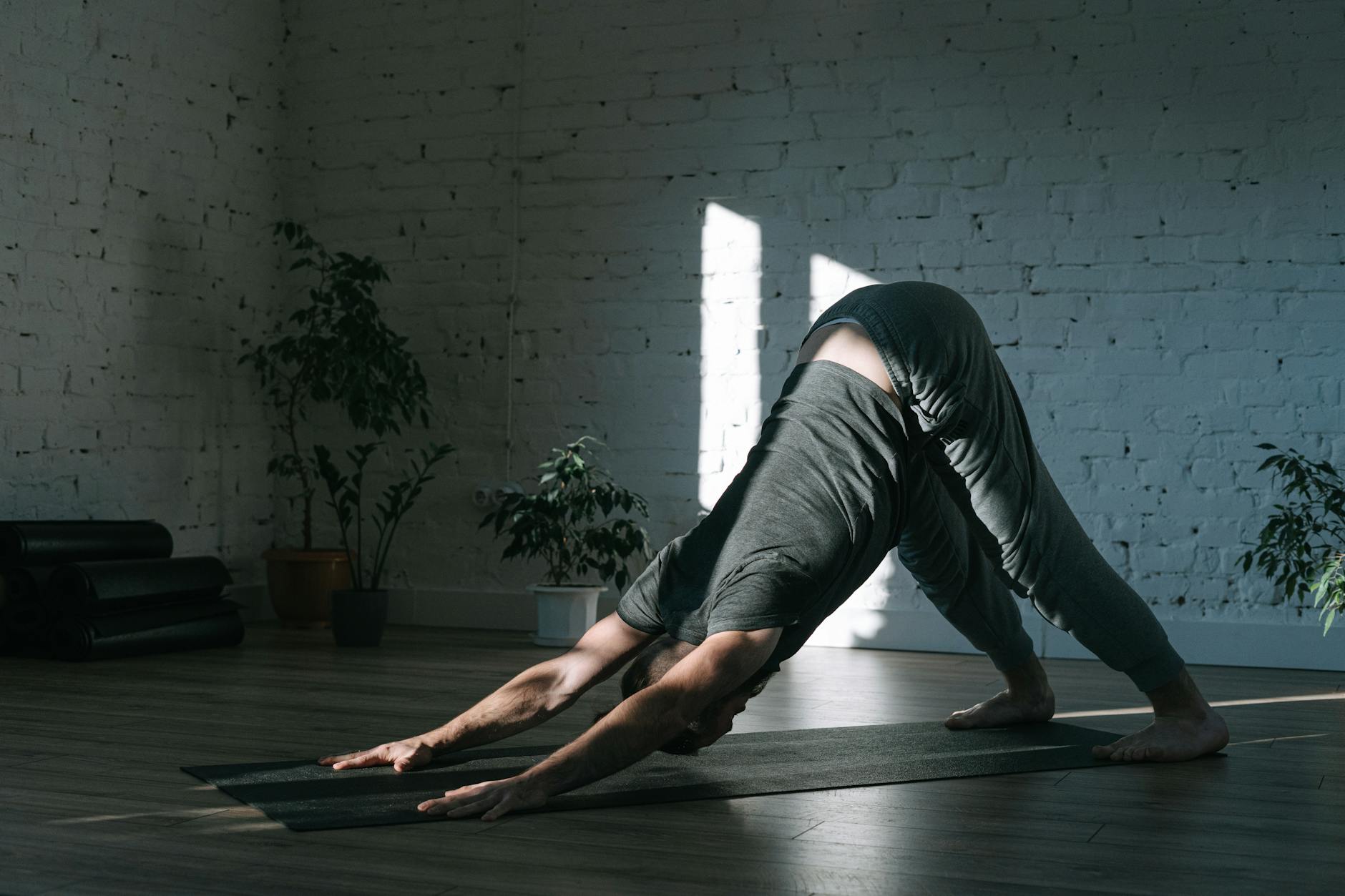 Adult man practicing yoga in downward dog pose on a mat indoors, emphasizing mindfulness and tranquility. - beginner yoga routine