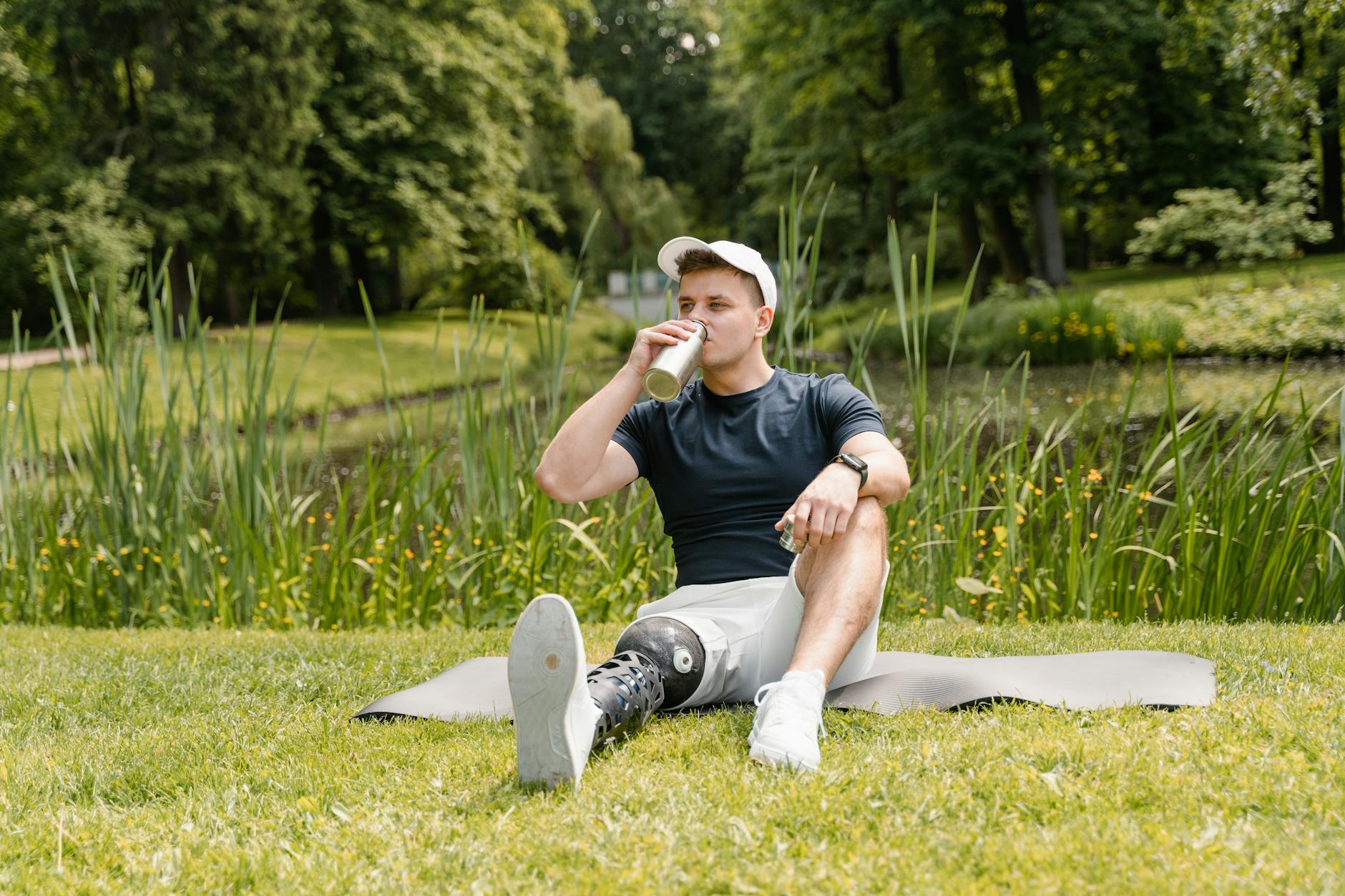 Man with a prosthetic leg drinks water on a mat in a tranquil park setting. - best recovery drink