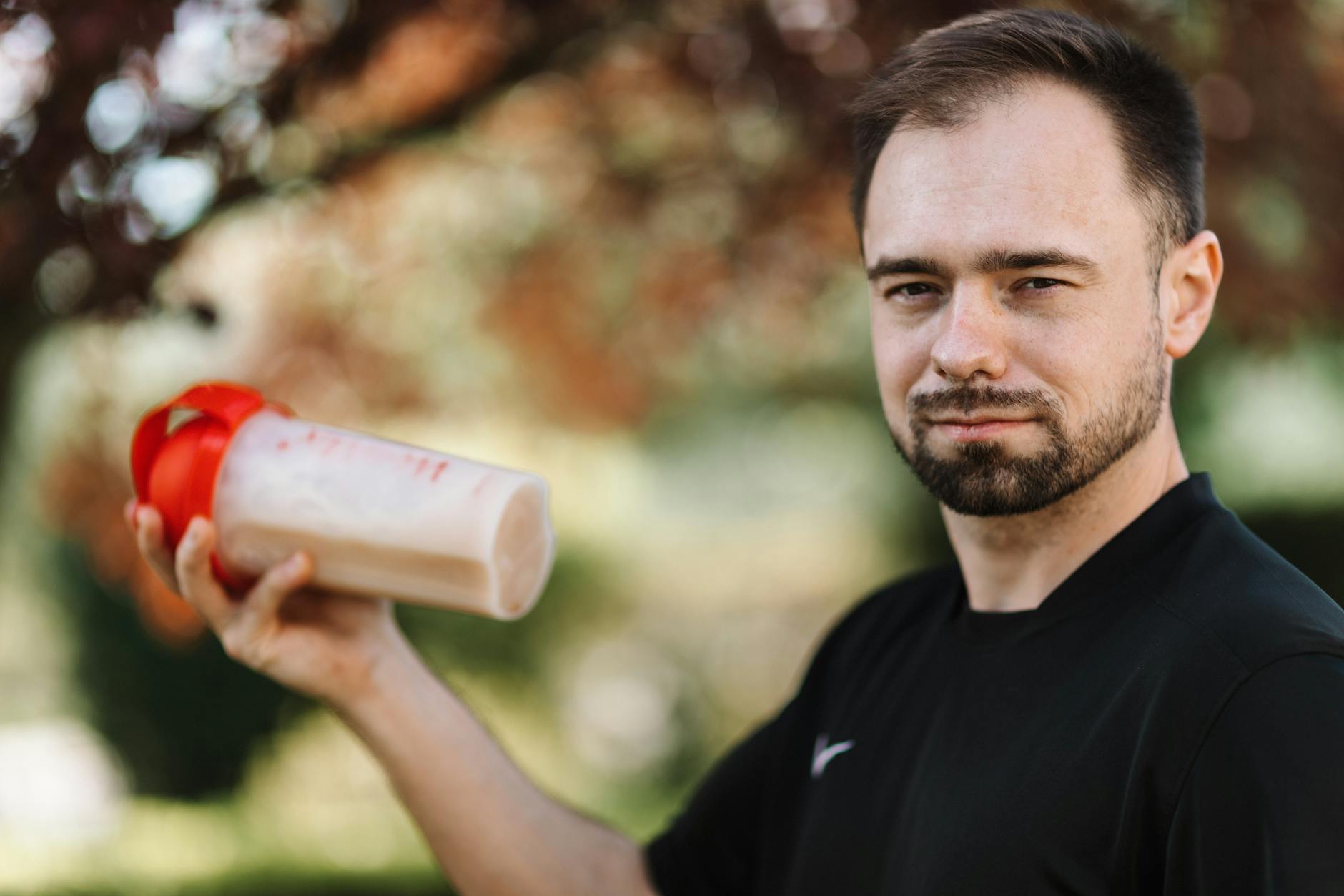 Adult man holding a protein shake outdoors during the day. - best recovery drink