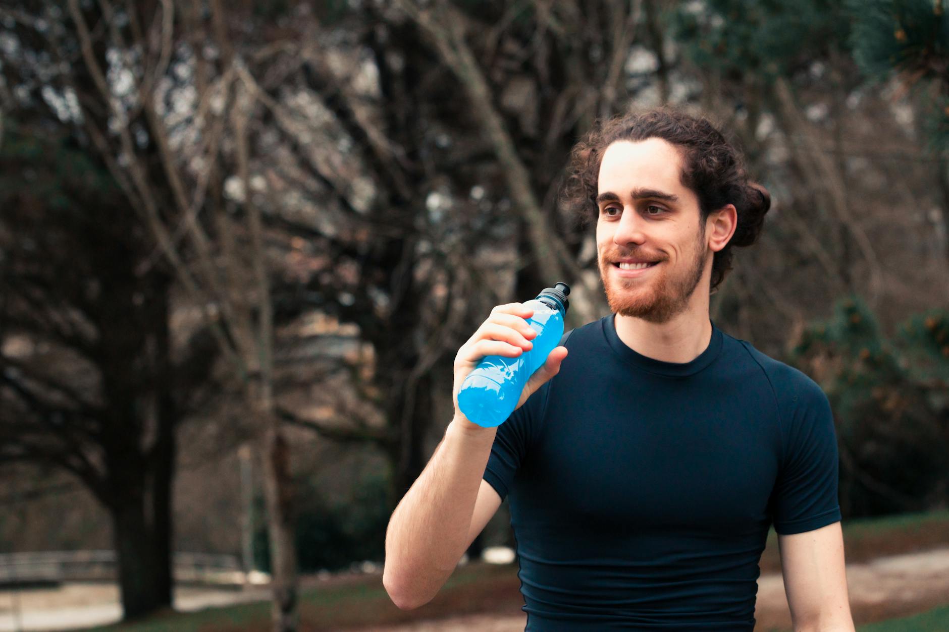 A young man enjoying a refreshing drink outdoors after a run, showcasing a healthy lifestyle. - best recovery drink