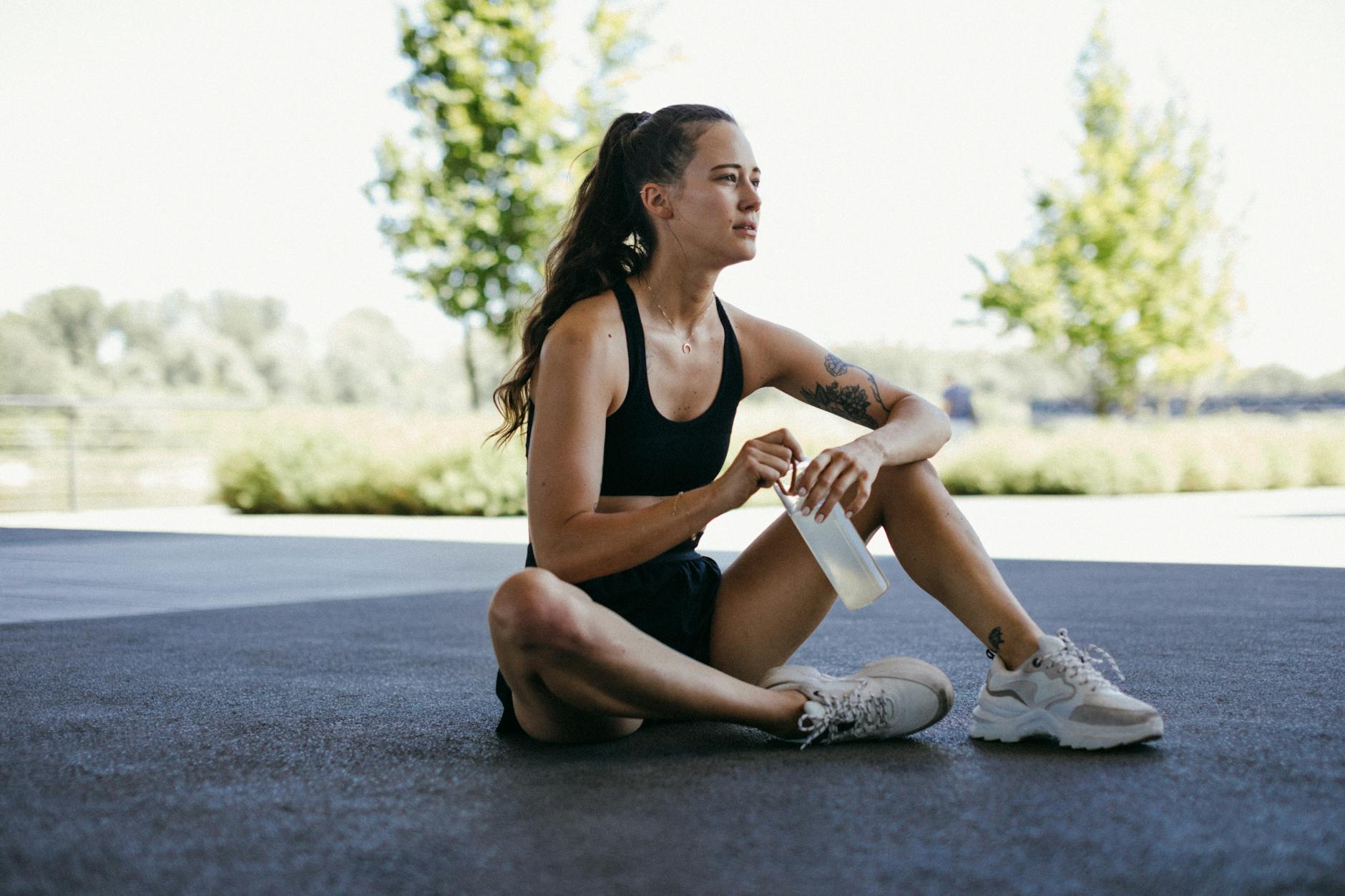 A young woman resting outdoors with a water bottle, taking a break after exercise. - best recovery drink