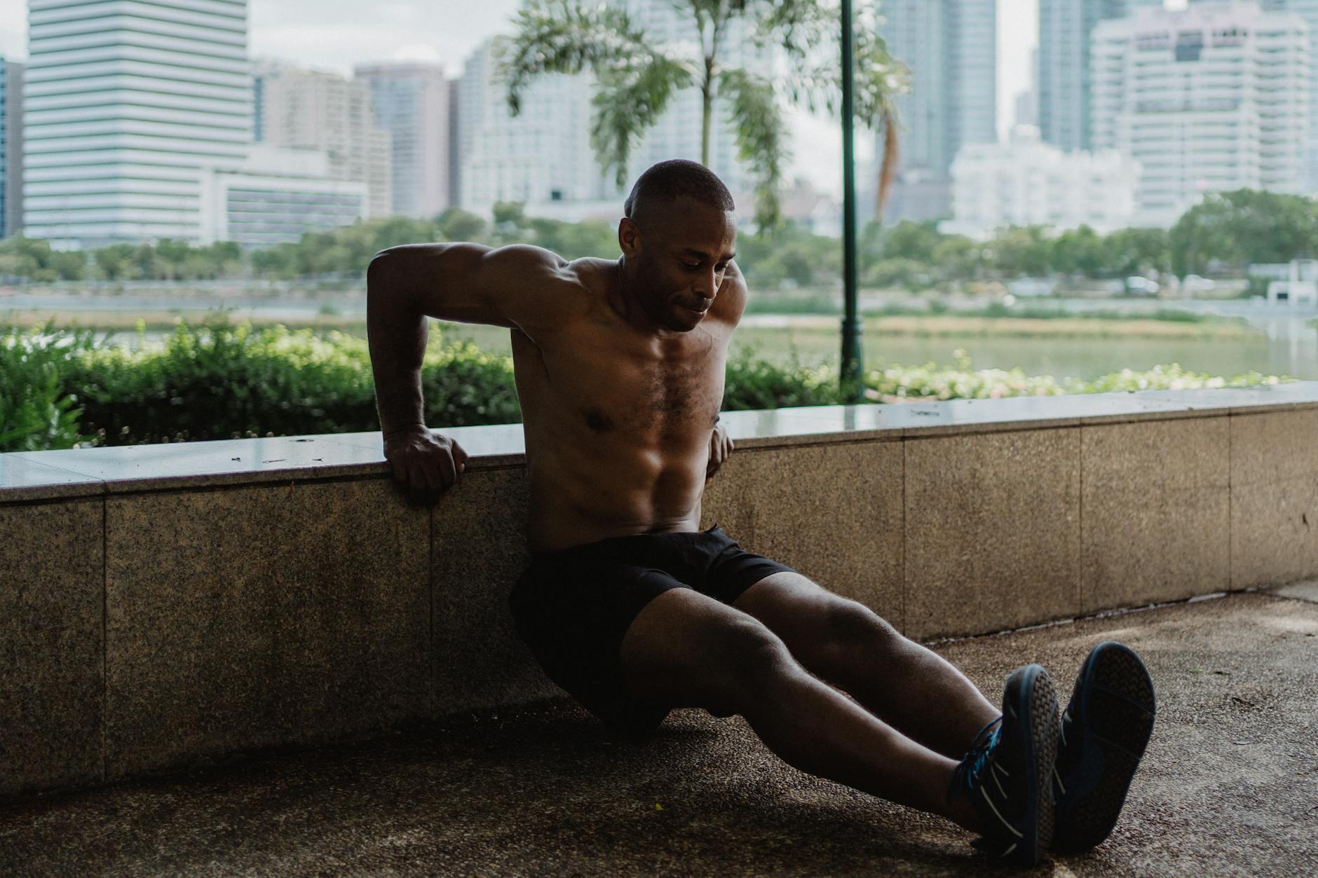 An athletic man engages in a tricep dip workout in an urban park setting. - bodyweight strength reset