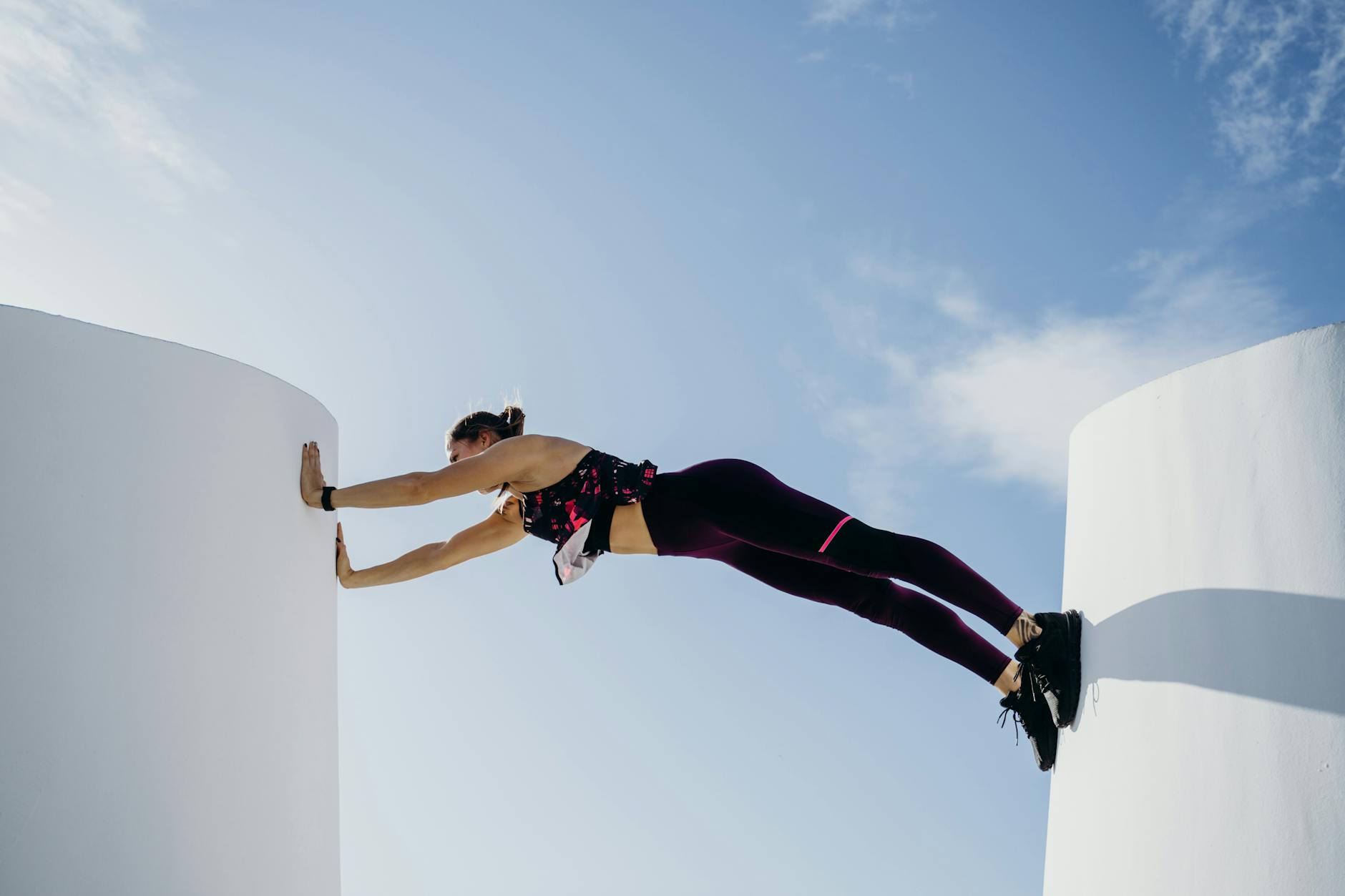 Strong woman balancing in plank position between two walls outdoors under a clear sky. - bodyweight strength reset