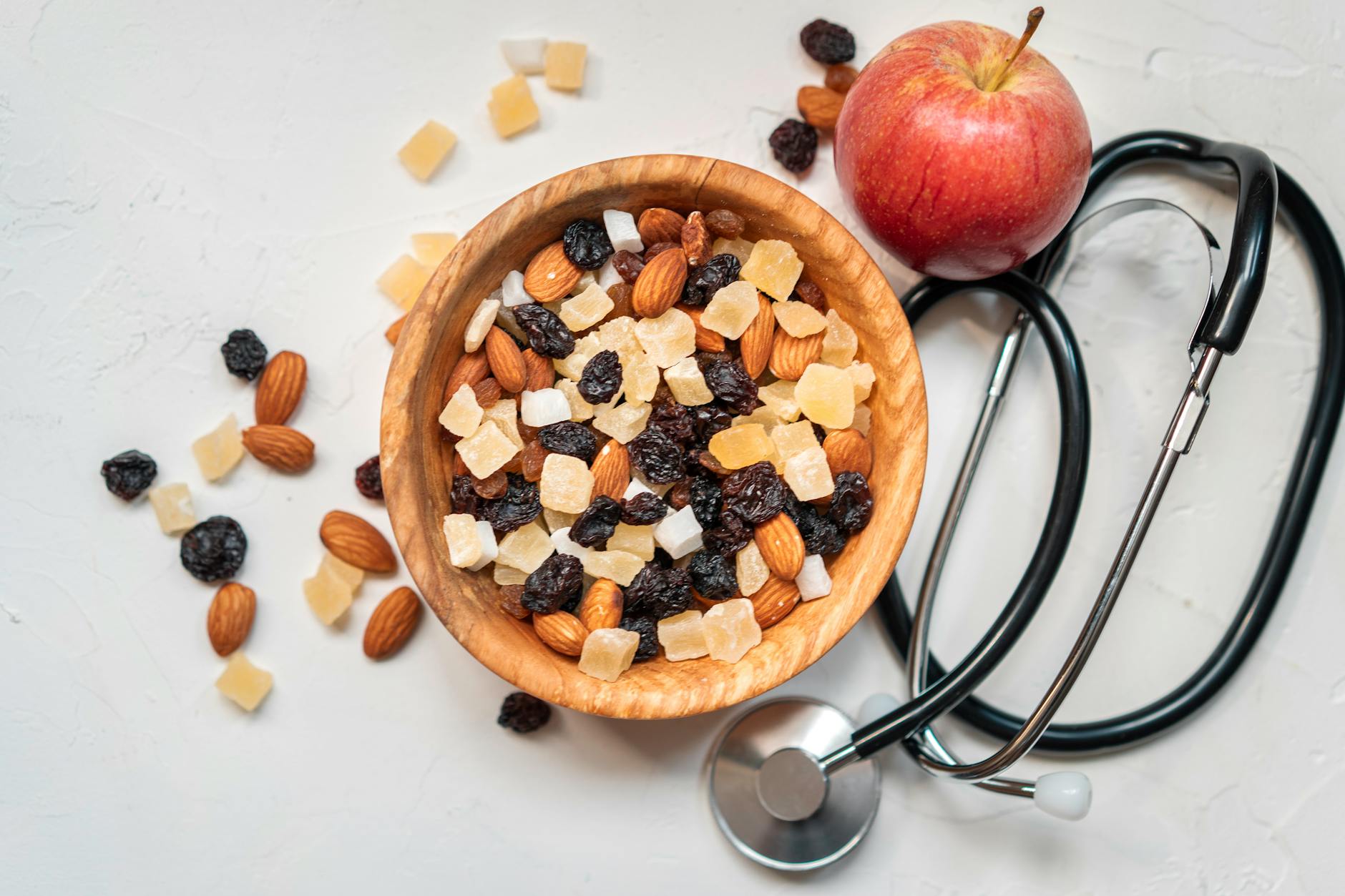 Top view of a mixed nut and dried fruit bowl with an apple and stethoscope, emphasizing healthy eating. - boost metabolism foods