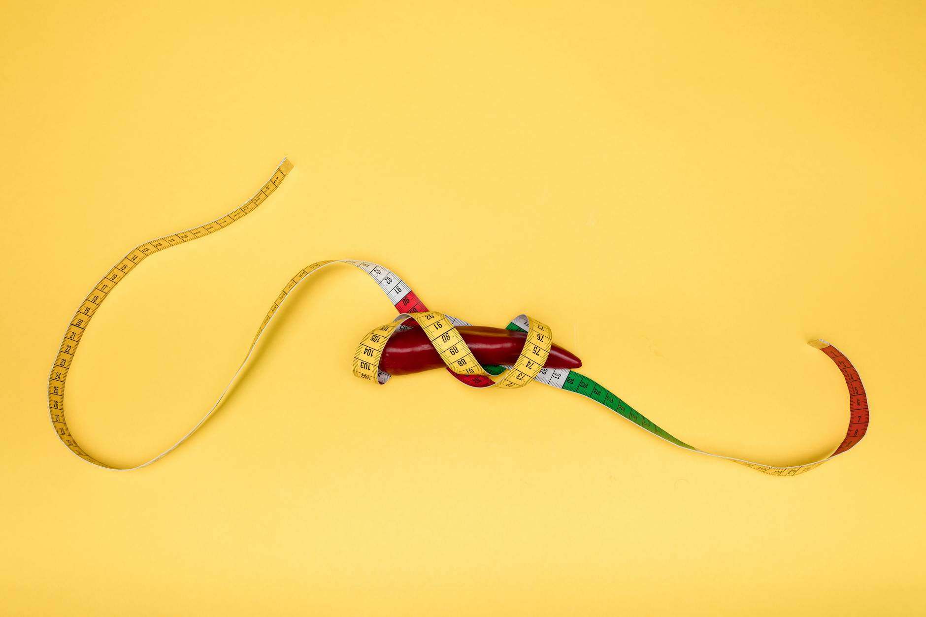 A red pepper wrapped in a colorful measuring tape, set against a bright yellow backdrop, symbolizing health and measurement. - boost metabolism naturally