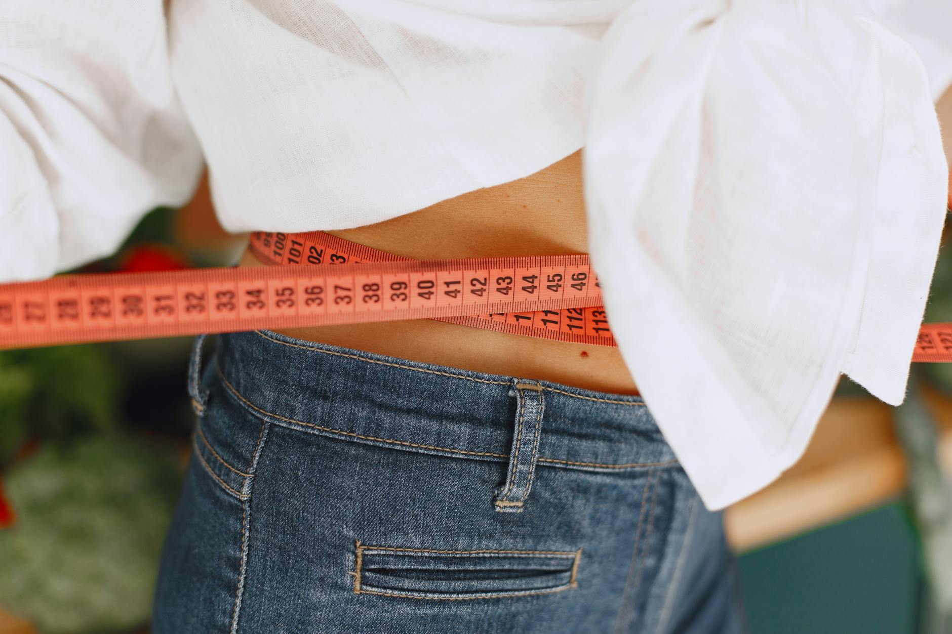 Close-up image of a woman measuring her waist with a tape measure, promoting fitness and health goals. - calorie deficit for weight loss