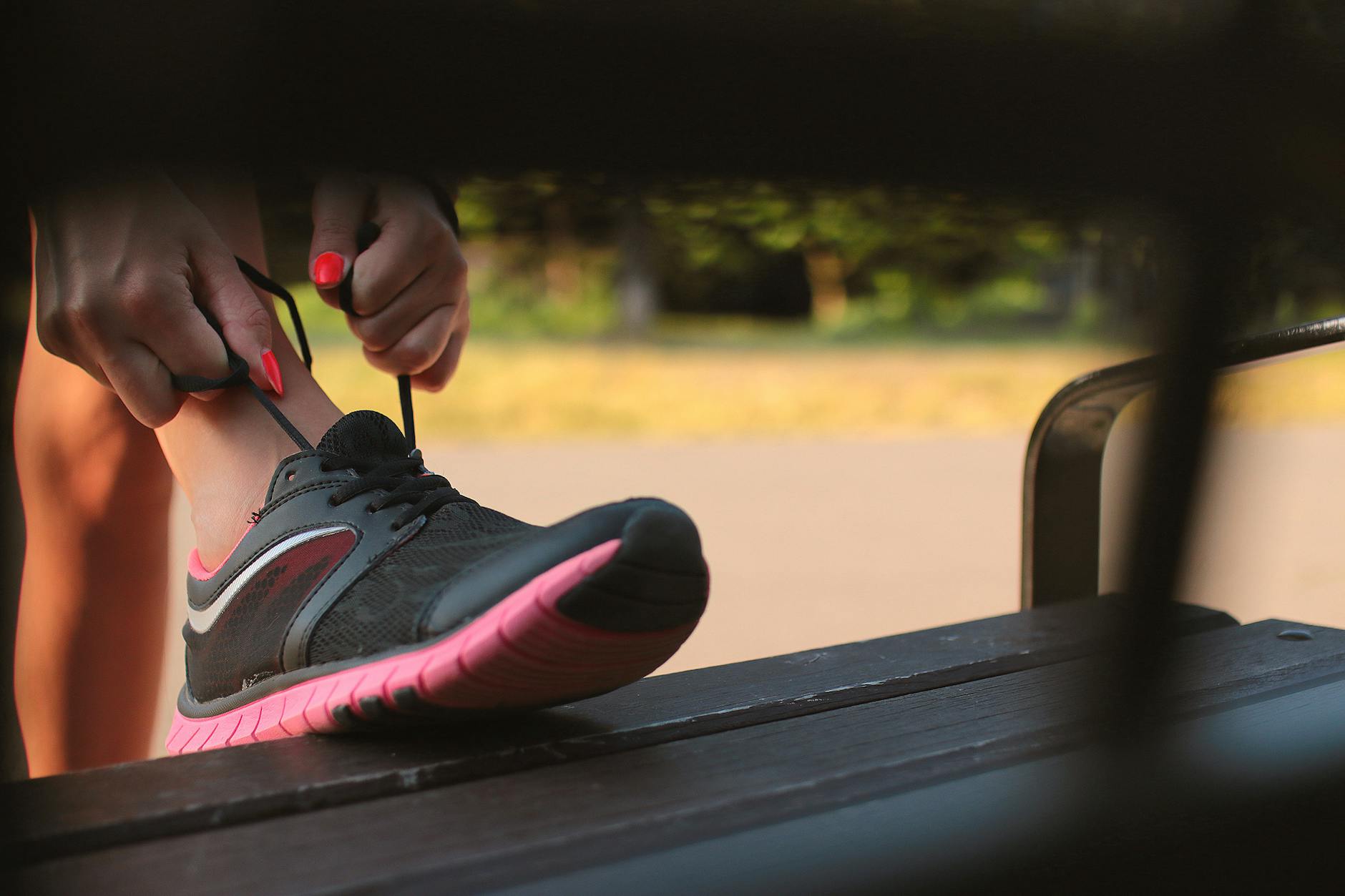 Close-up of a woman tying her athletic shoes on a bench in a park, preparing for a run. - couch to 5k spring