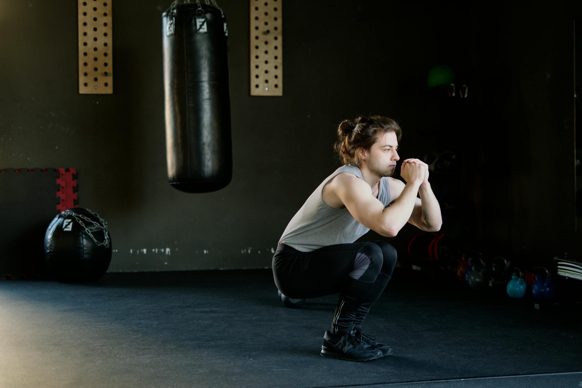A man is doing squats in a gym with a punching bag. The setting appears stylish and focused on fitness. - no equipment workouts