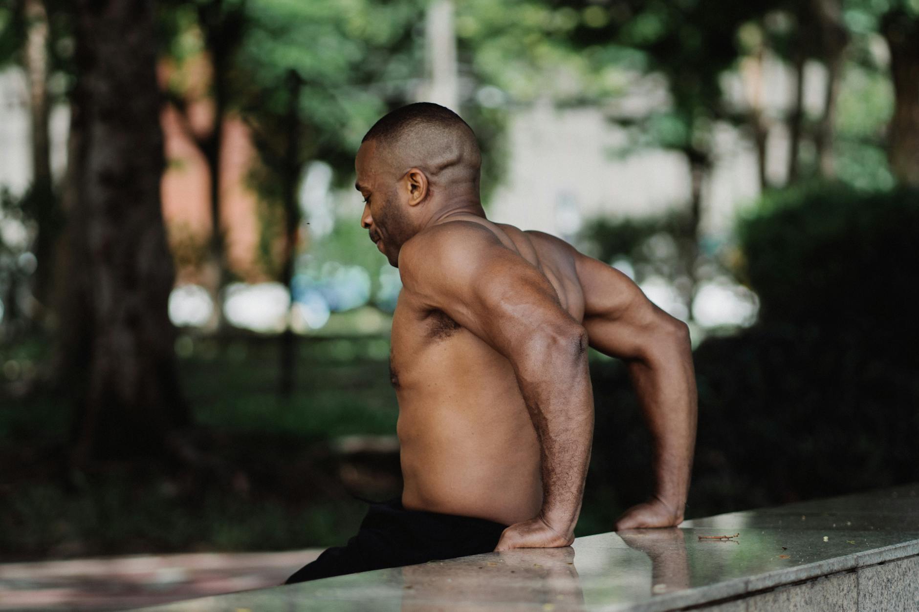 Shirtless man performing tricep dips in a park, showcasing outdoor fitness and healthy lifestyle. - full body fat burn