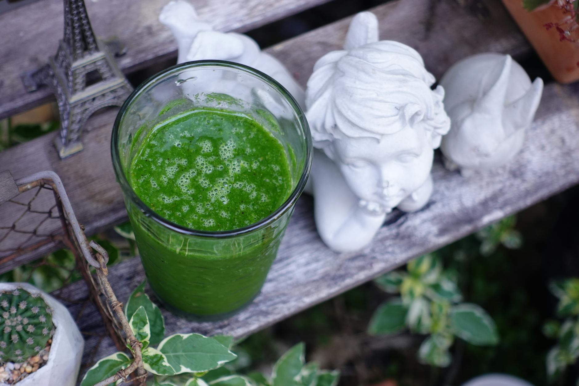 A vibrant green smoothie next to angel statue and Eiffel Tower model outdoors. - gentle spring detox