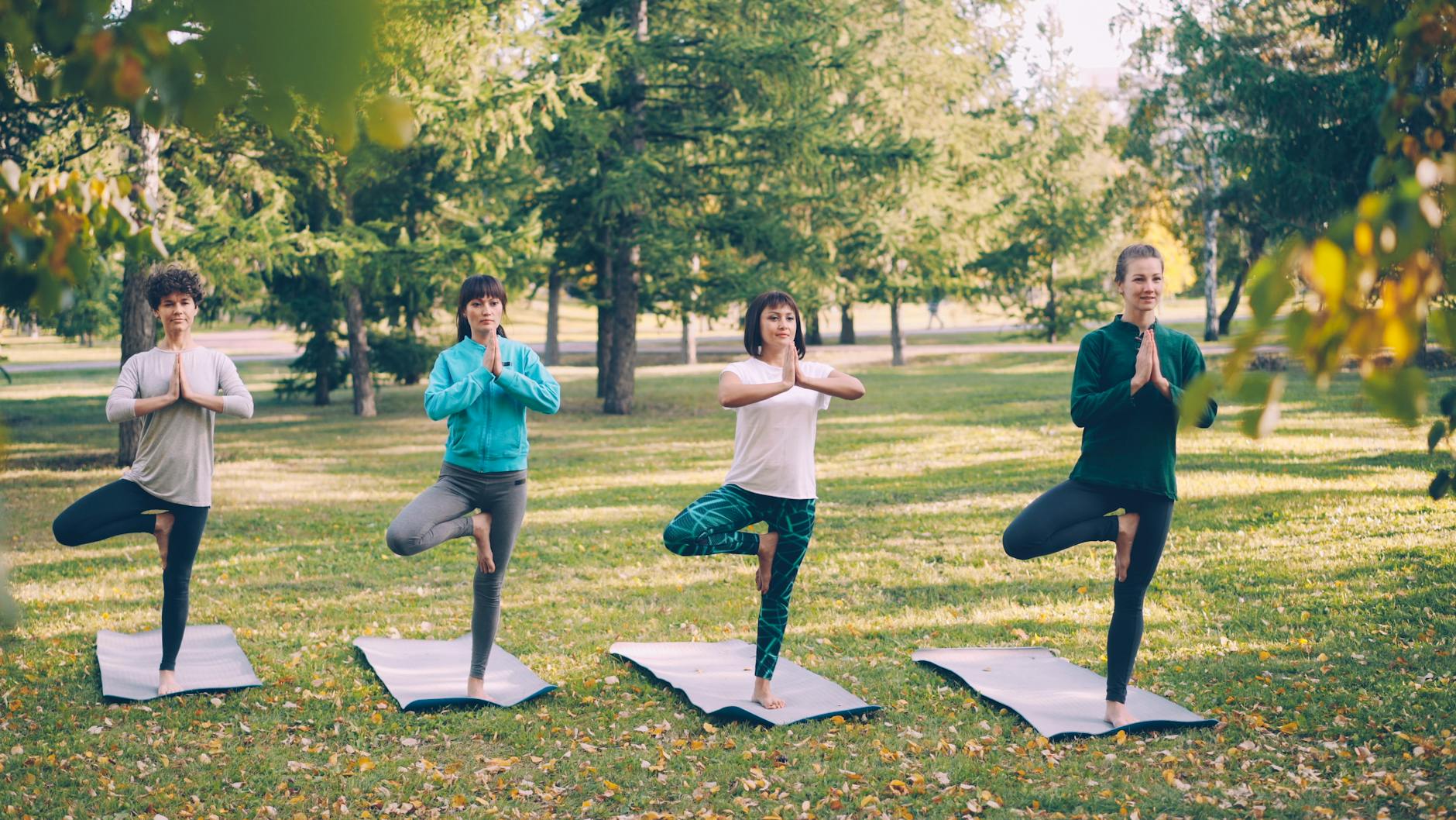 Four people practice yoga together outdoors in the park during daytime. - gentle yoga spring
