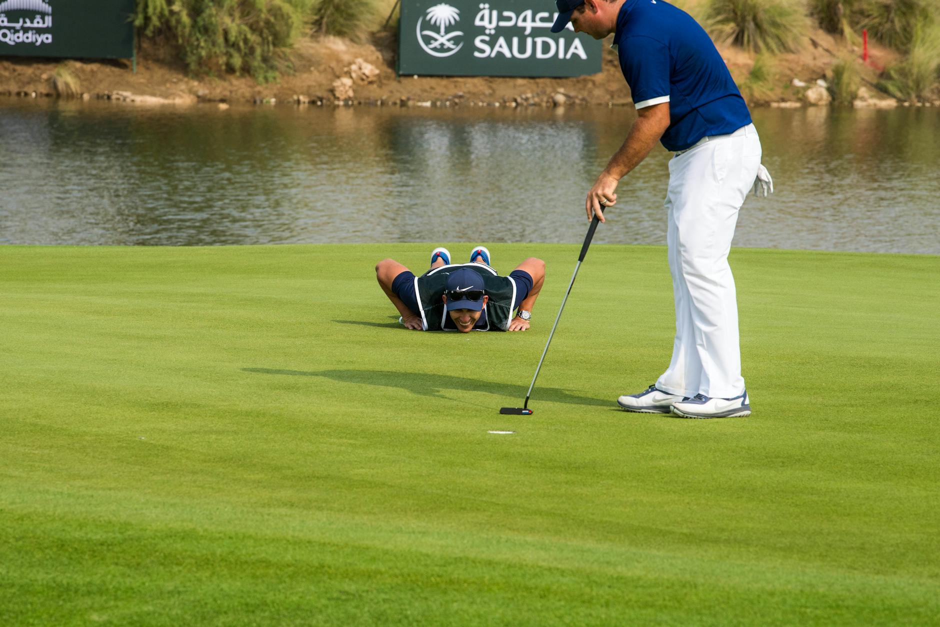 Two golfers on a green, focusing on a putt by a pond, showcasing teamwork and precision. - golf flexibility exercises