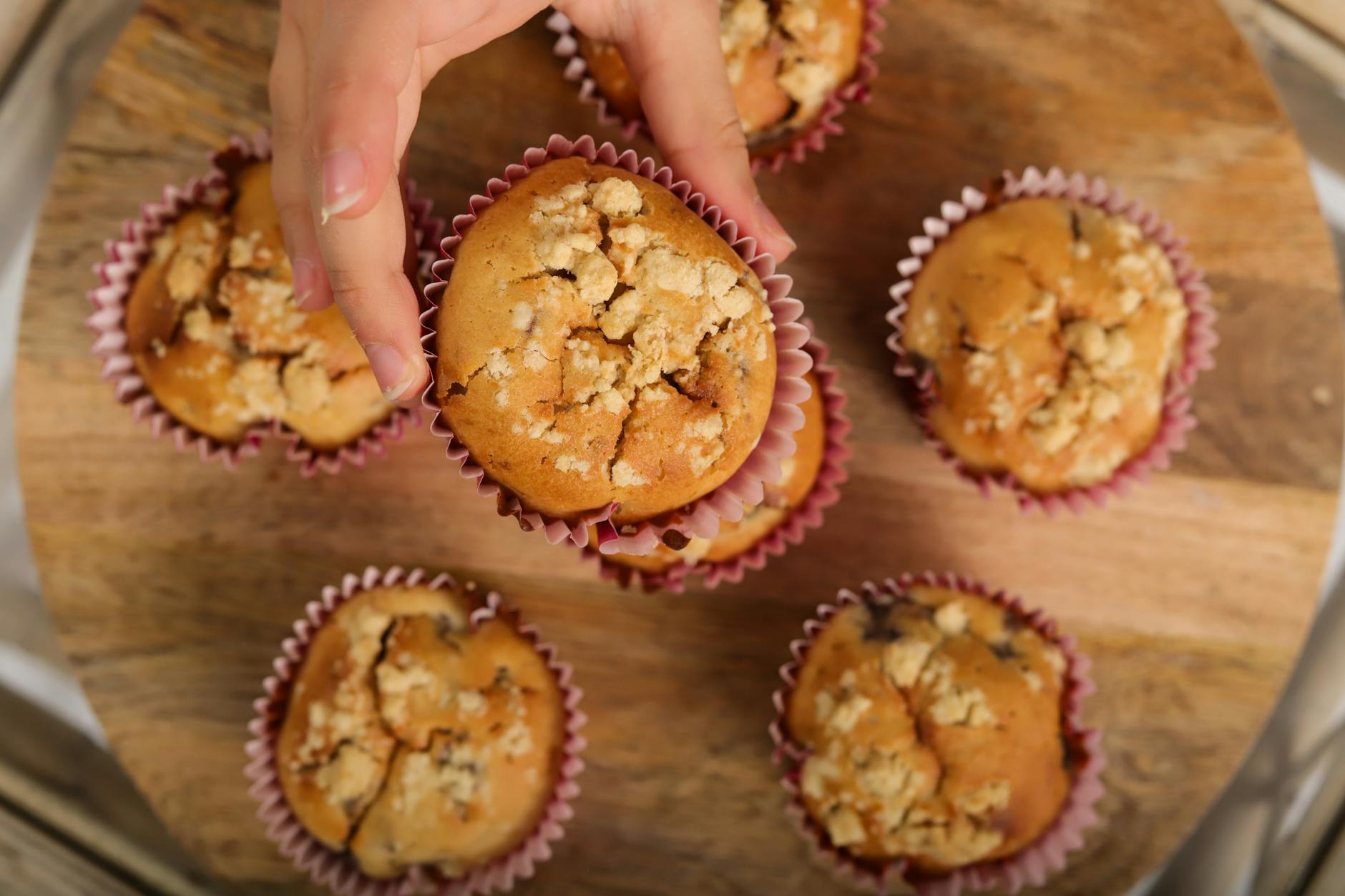 Hand picking a freshly baked muffin from a group on a wooden platter. - healthy breakfast muffins