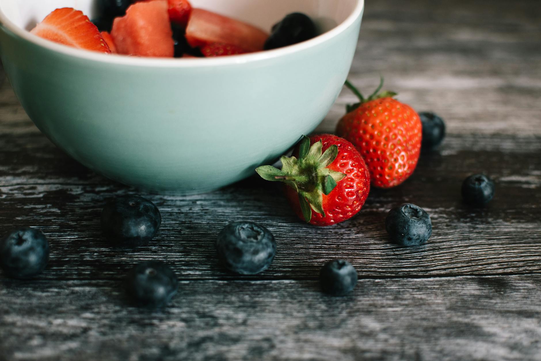 Close-up of fresh strawberries and blueberries in a ceramic bowl on a rustic wooden table. - healthy spring snacks