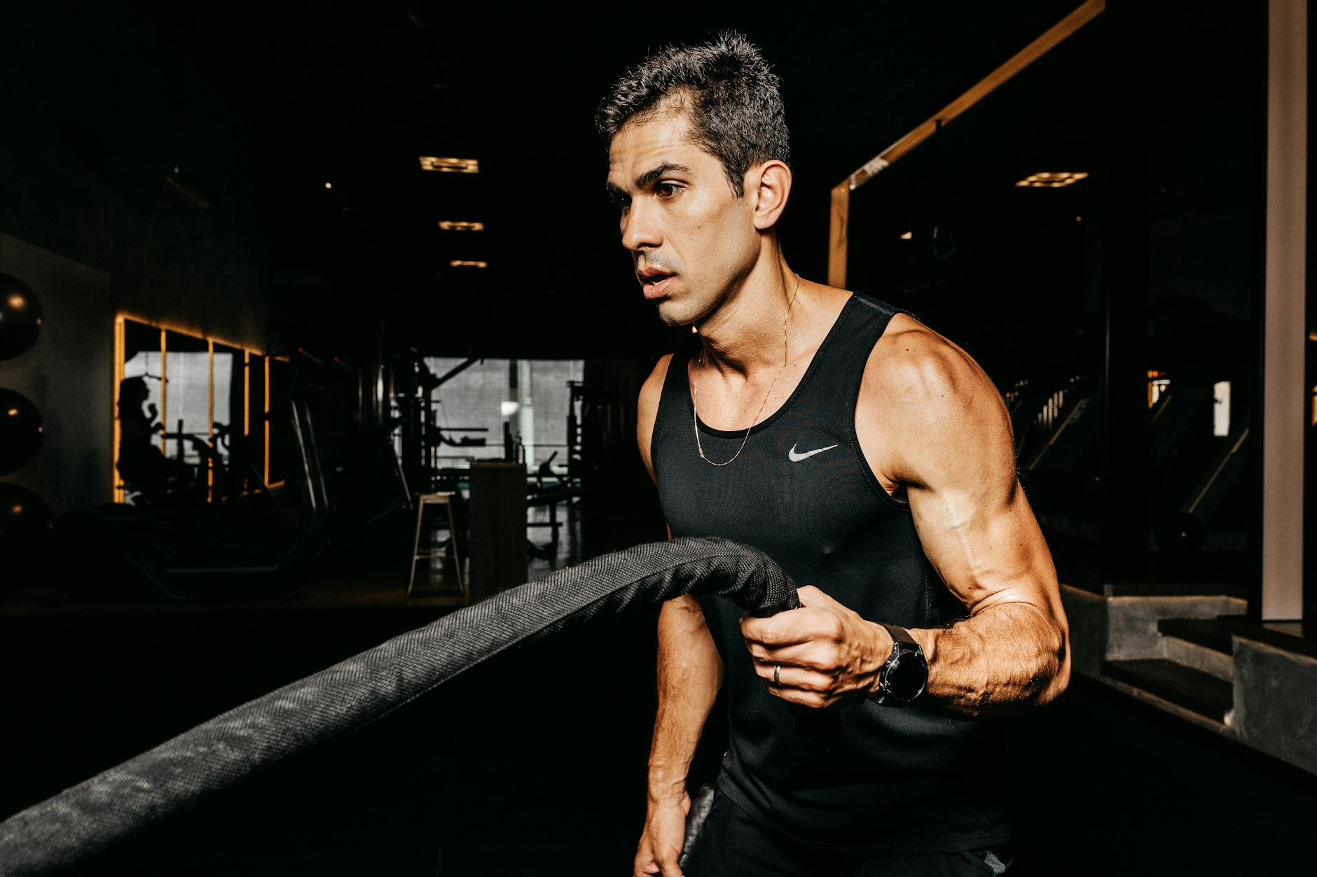 A determined male athlete working out with battle ropes in a dimly lit gym, showcasing strength and fitness. - hiit for busy people