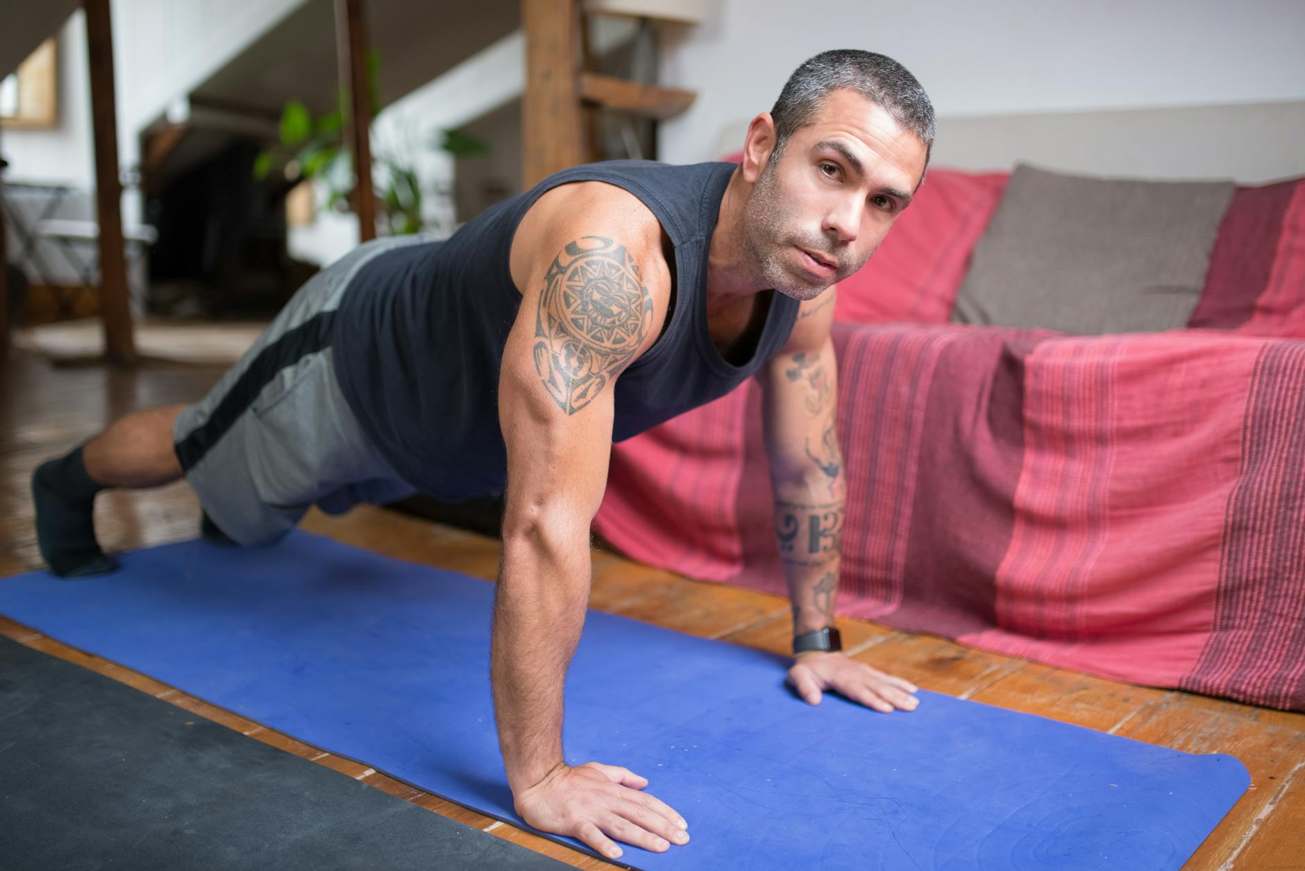 A tattooed man performs push-ups on a yoga mat indoors, focusing on fitness training. - at home strength